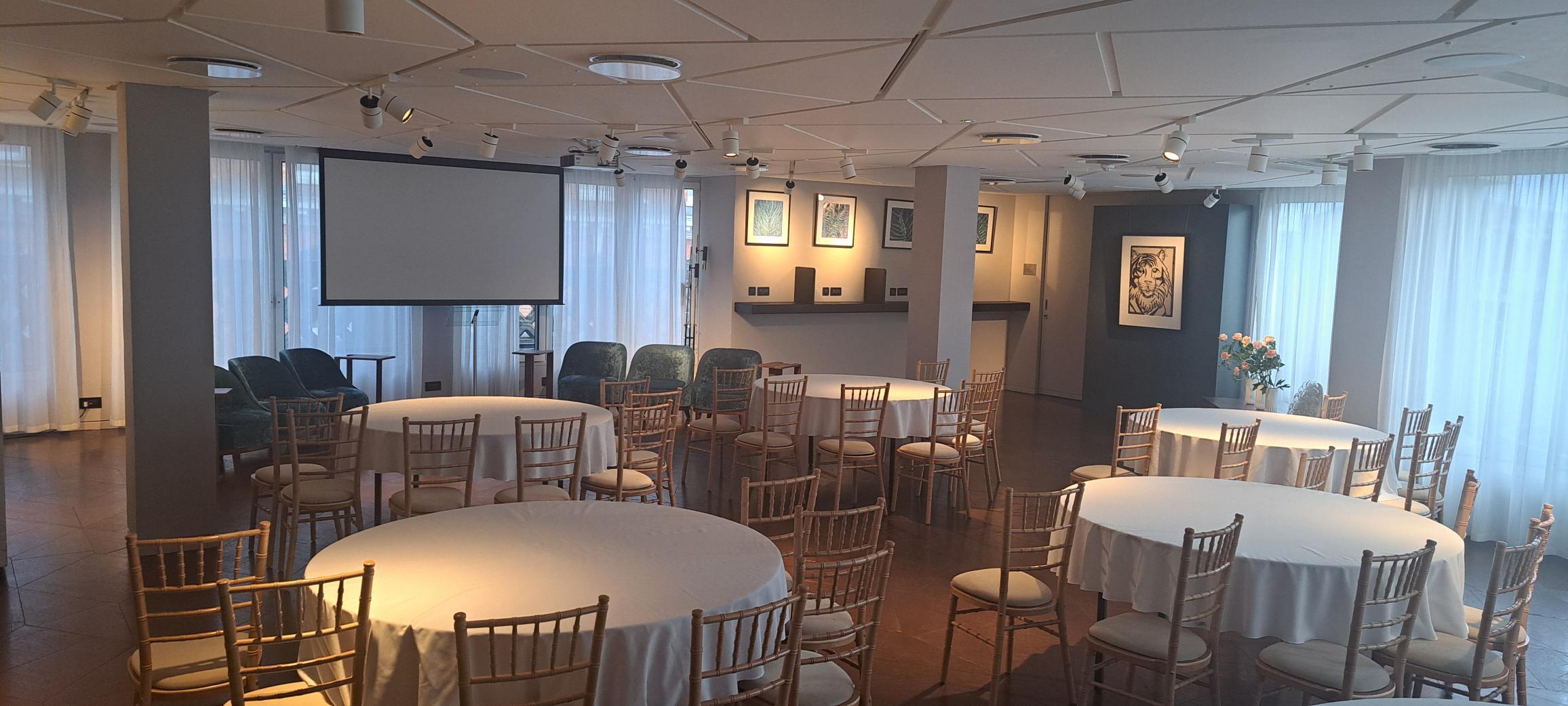 The Lounge at 12 Hay Hill: elegant meeting space with circular tables and projector screen.