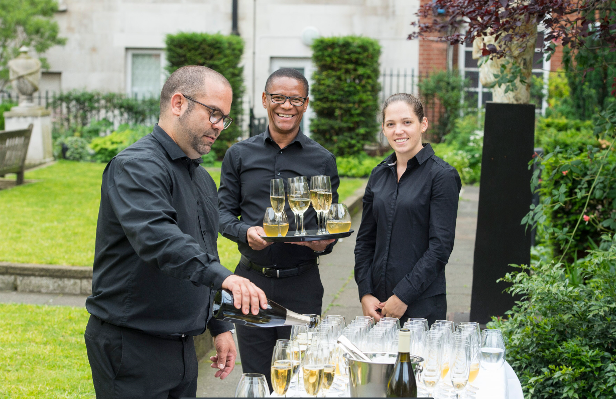 Southwood Garden event with elegant staff serving champagne in lush greenery.