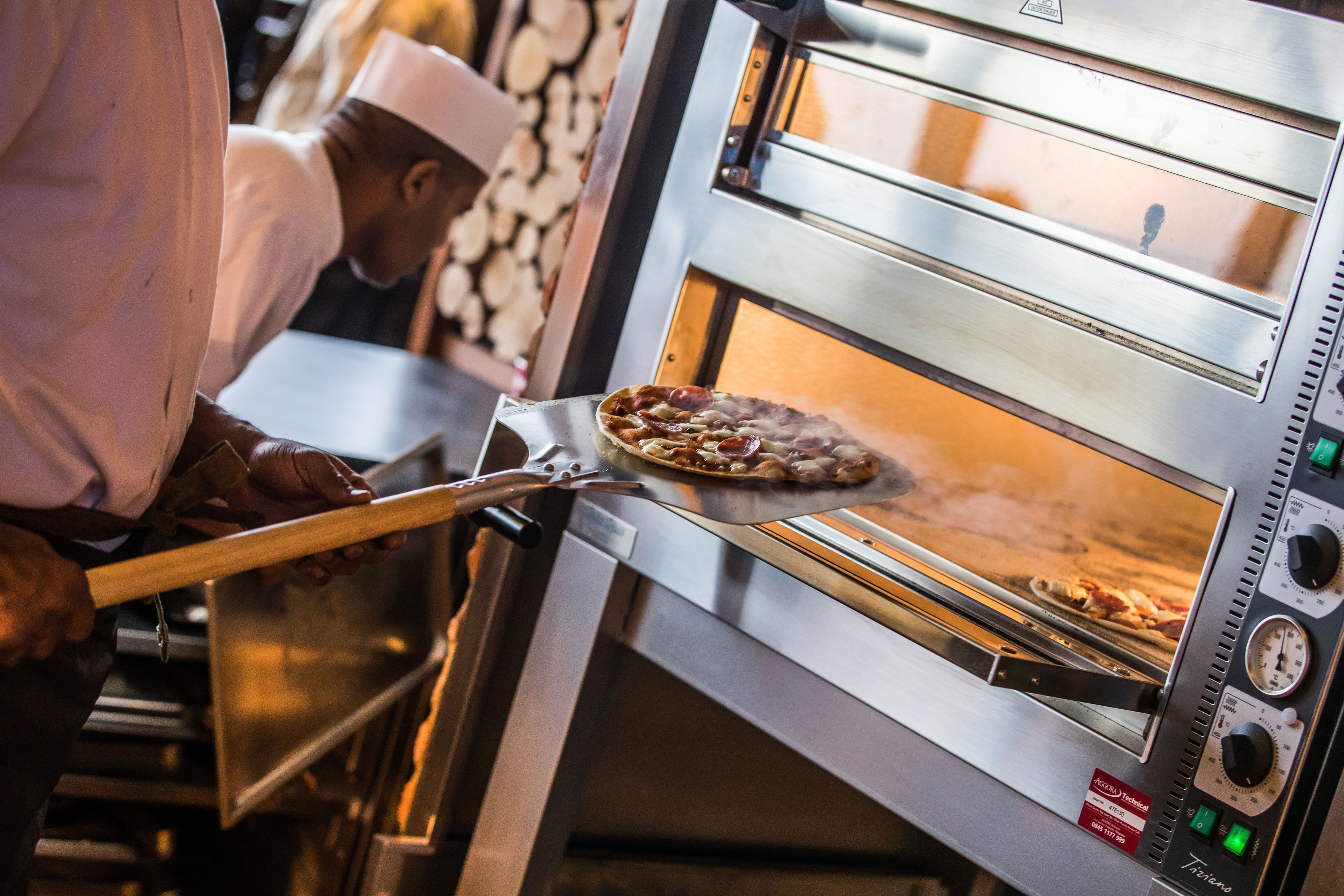 Chef pulling pizza from oven at British Airways Rose Garden, Twickenham event catering.