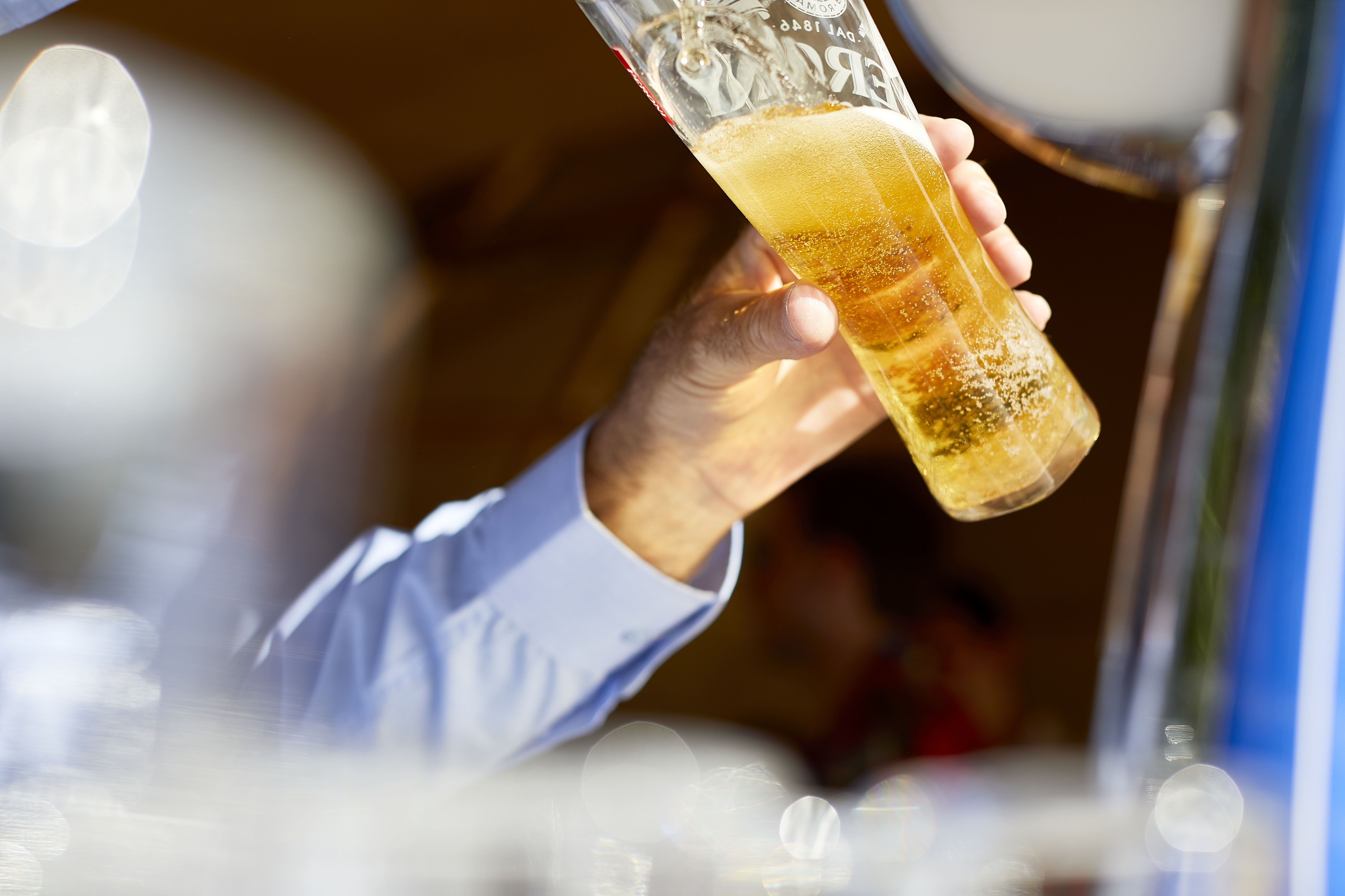 Hand holding a tall beer glass at Lifehouse Spa gardens for event planning.