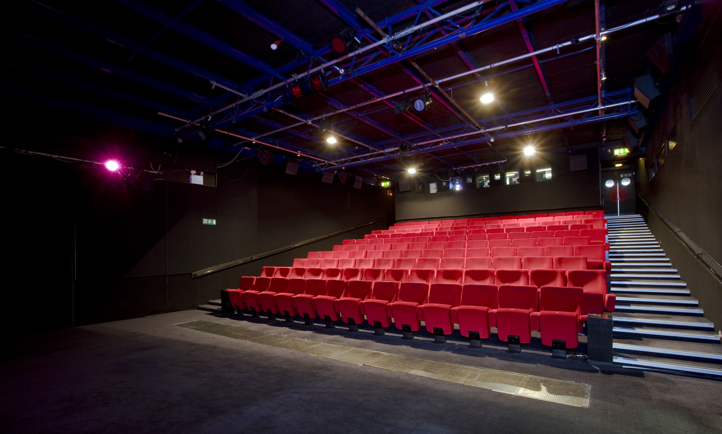 Versatile theater space with tiered red seating for corporate events and performances.