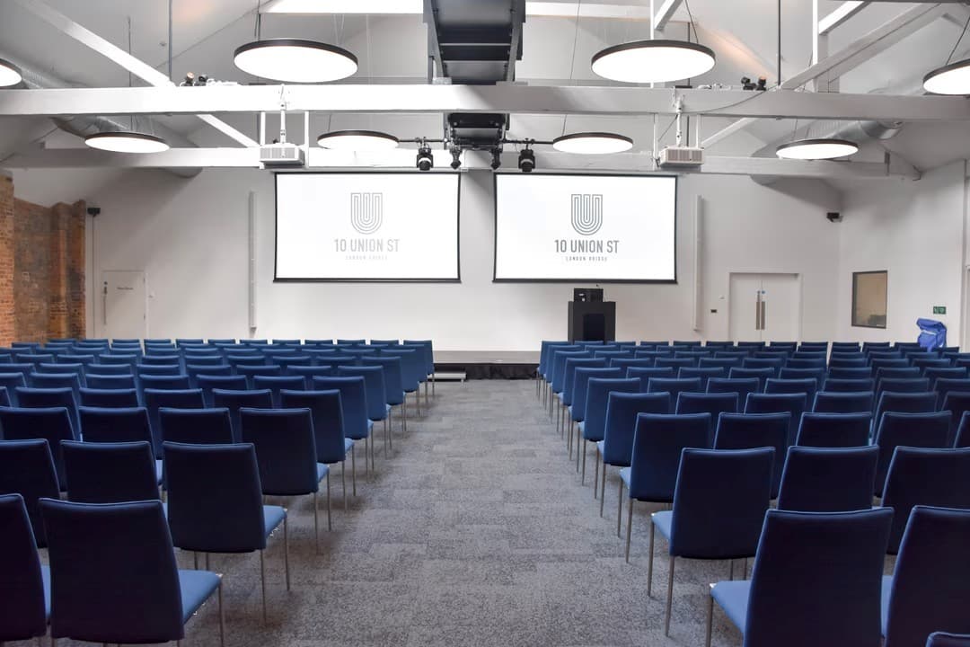 Industrial-chic Main Hall with dual-screen theater setup for corporate events and conferences.
