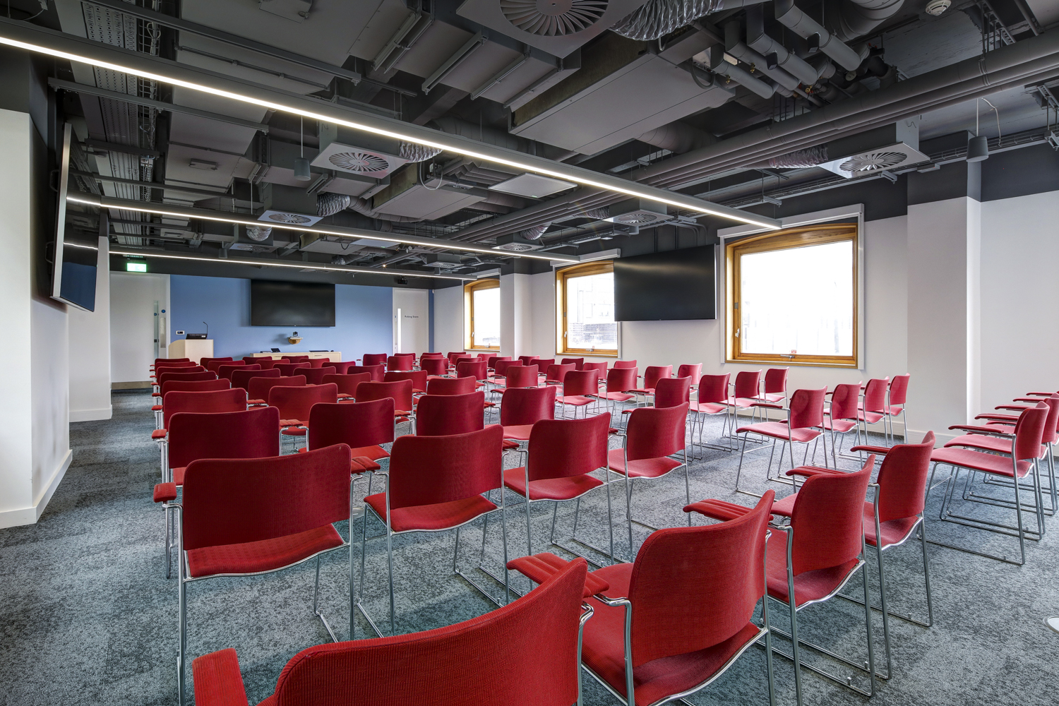 Modern meeting room with red chairs and dual screens for presentations and workshops.