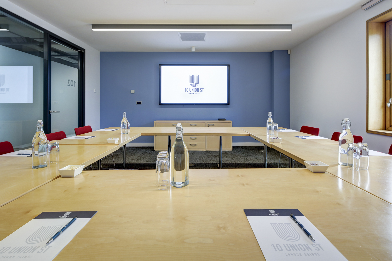 Modern meeting room with wooden table and red chairs, perfect for corporate workshops.