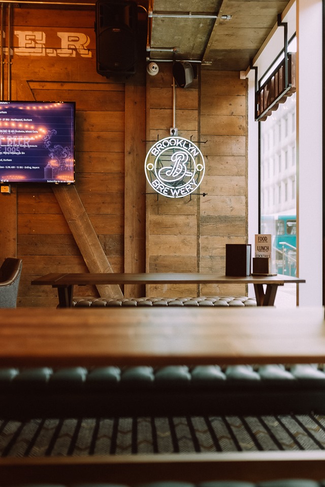 Stylish meeting space with rustic wood and neon Brooklyn Brewery sign, ideal for gatherings.