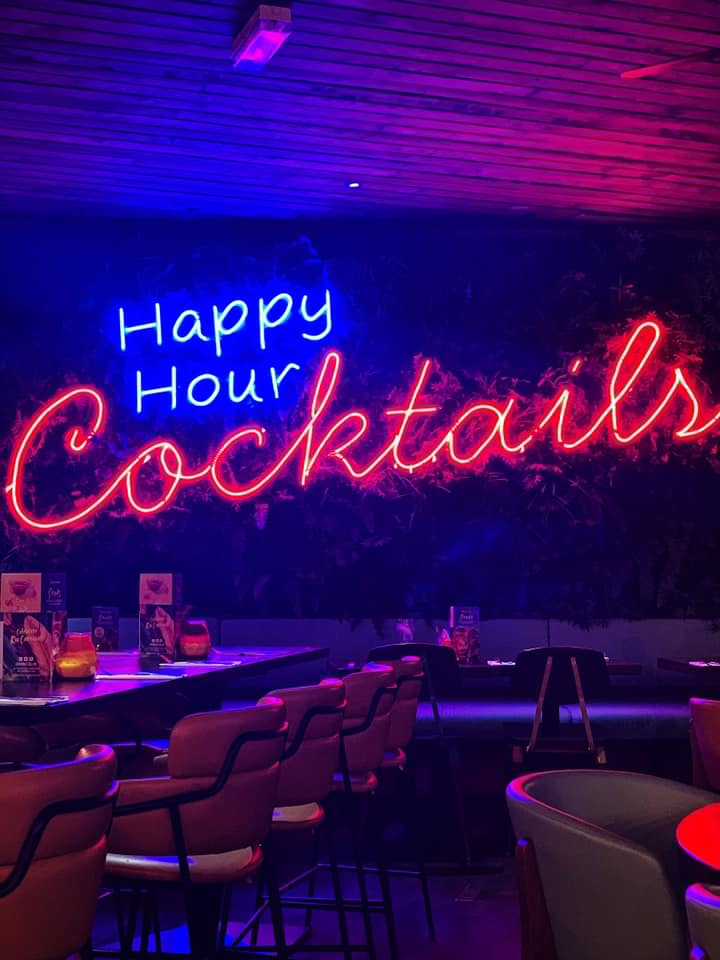 Vibrant neon "Happy Hour Cocktails" sign at Las Iguanas, ideal for networking events.