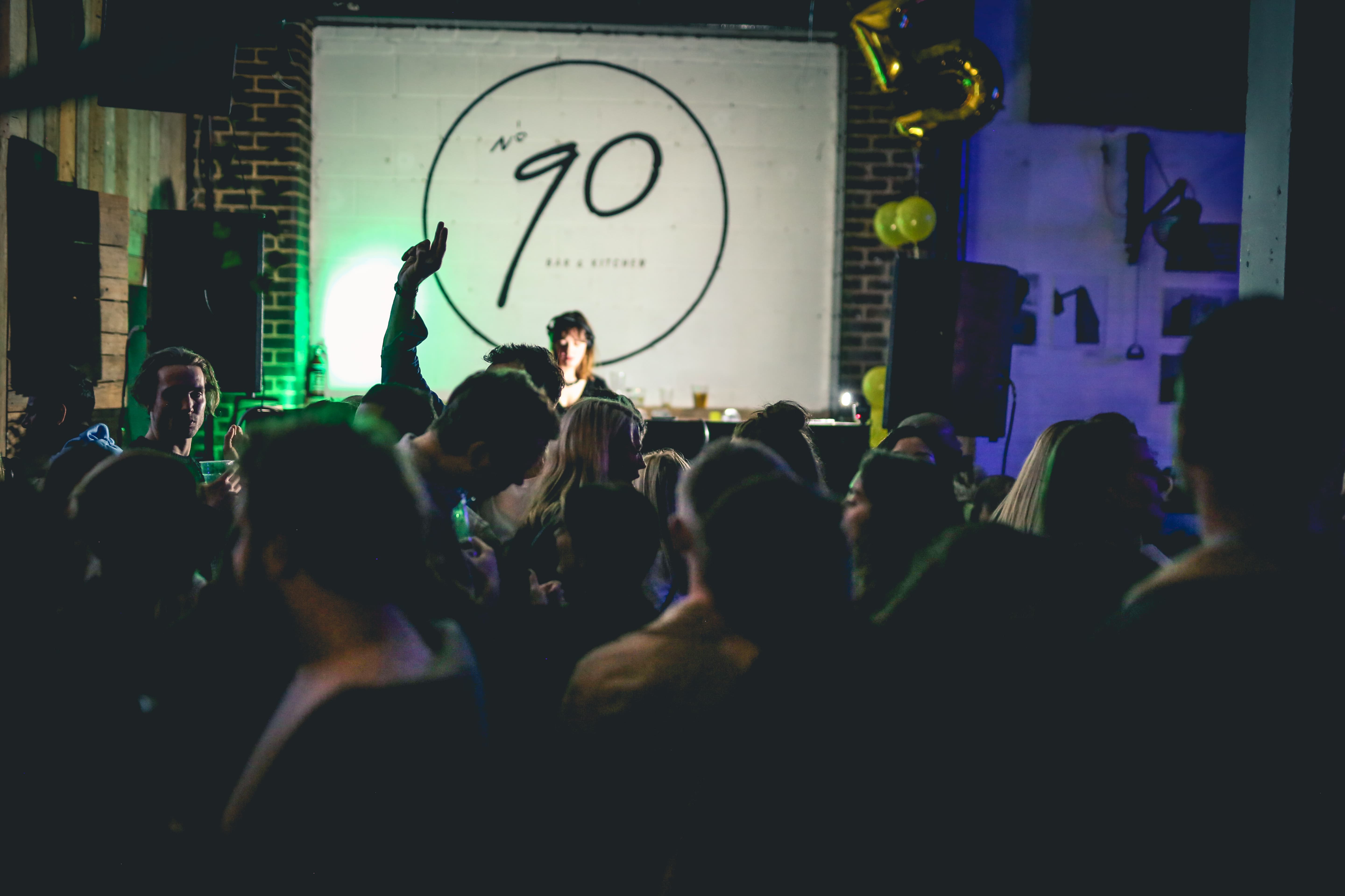 Lively networking event at 90 Bar & Kitchen with vibrant crowd and creative lighting.