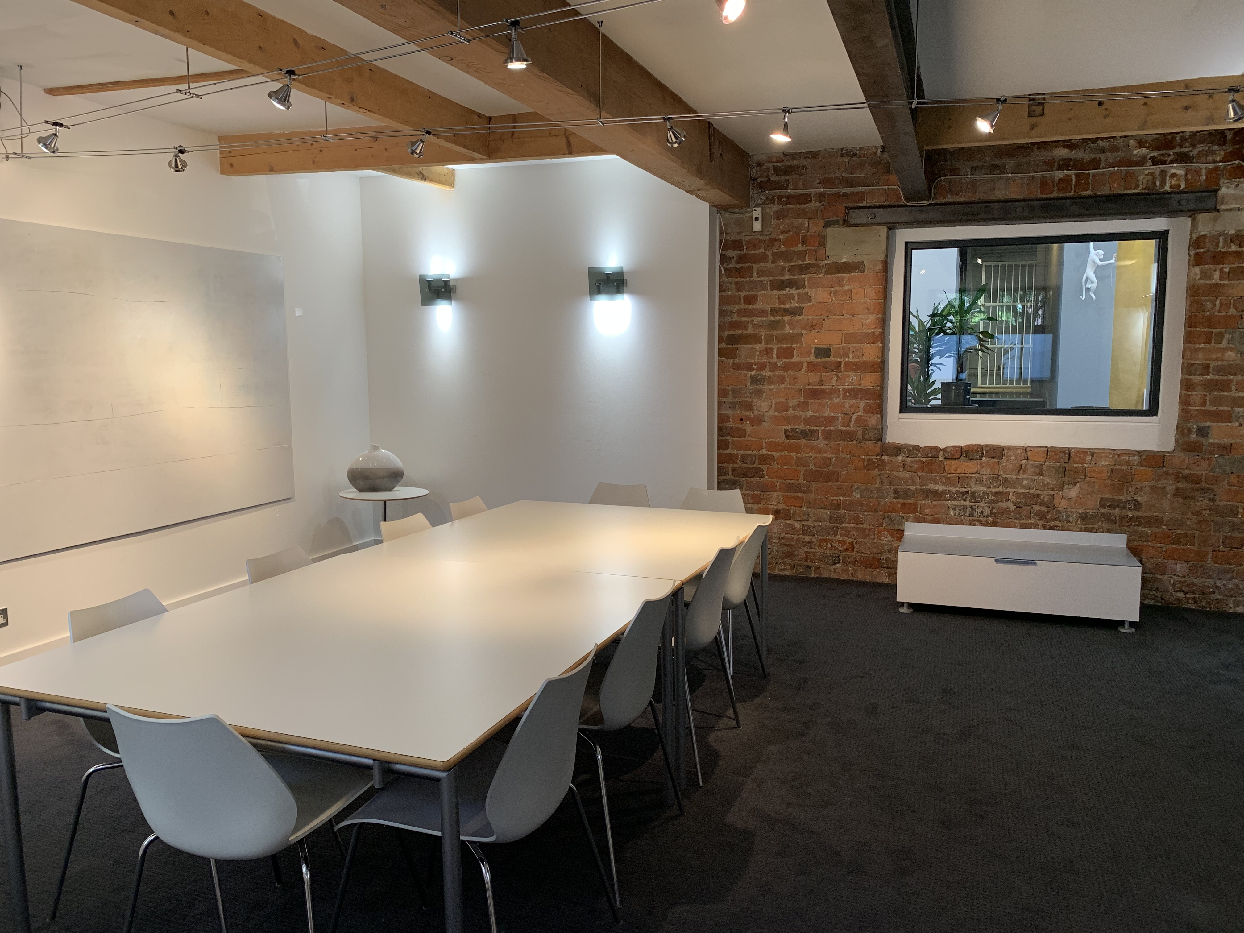 Modern meeting room with white table, exposed brick wall, ideal for collaborative sessions.