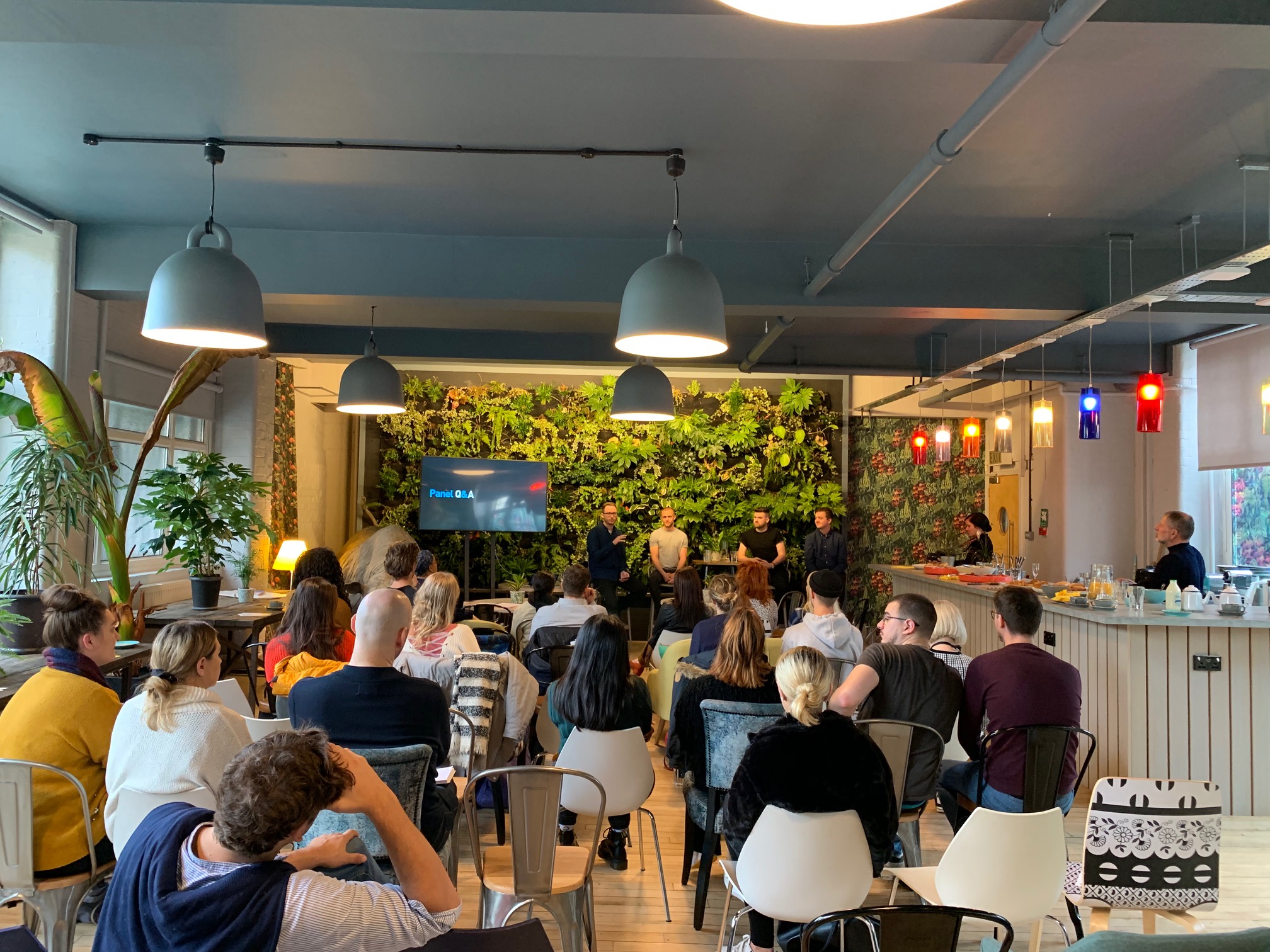 Vibrant Use.Cafe event space with green wall for panel discussion and refreshments.