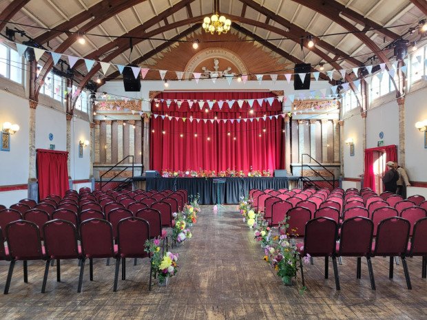 Stanley Hall event space with red chairs, stage, and floral decor for presentations or ceremonies.