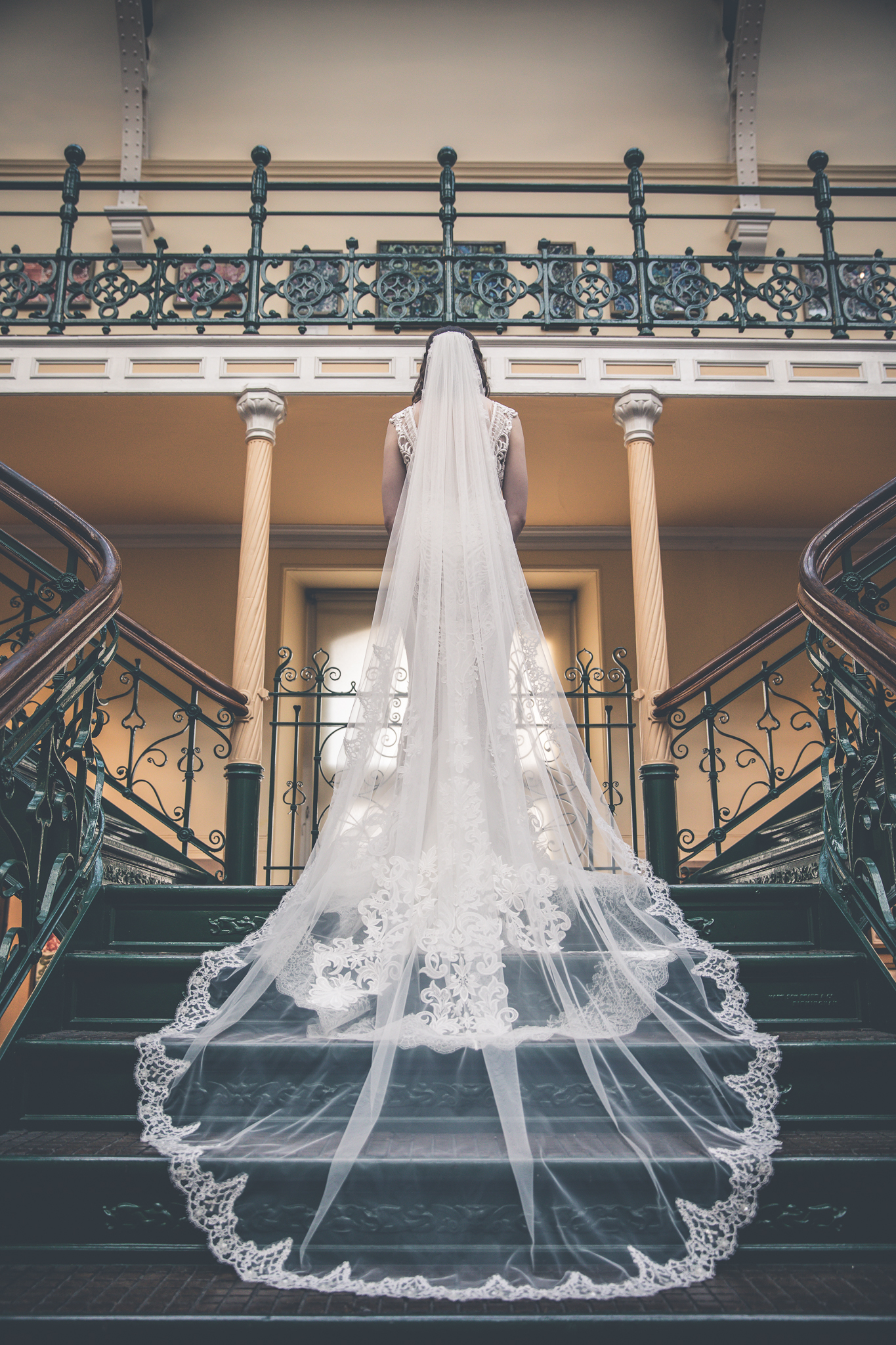 Bride in elegant gown on grand staircase at Birmingham Museum for wedding events.