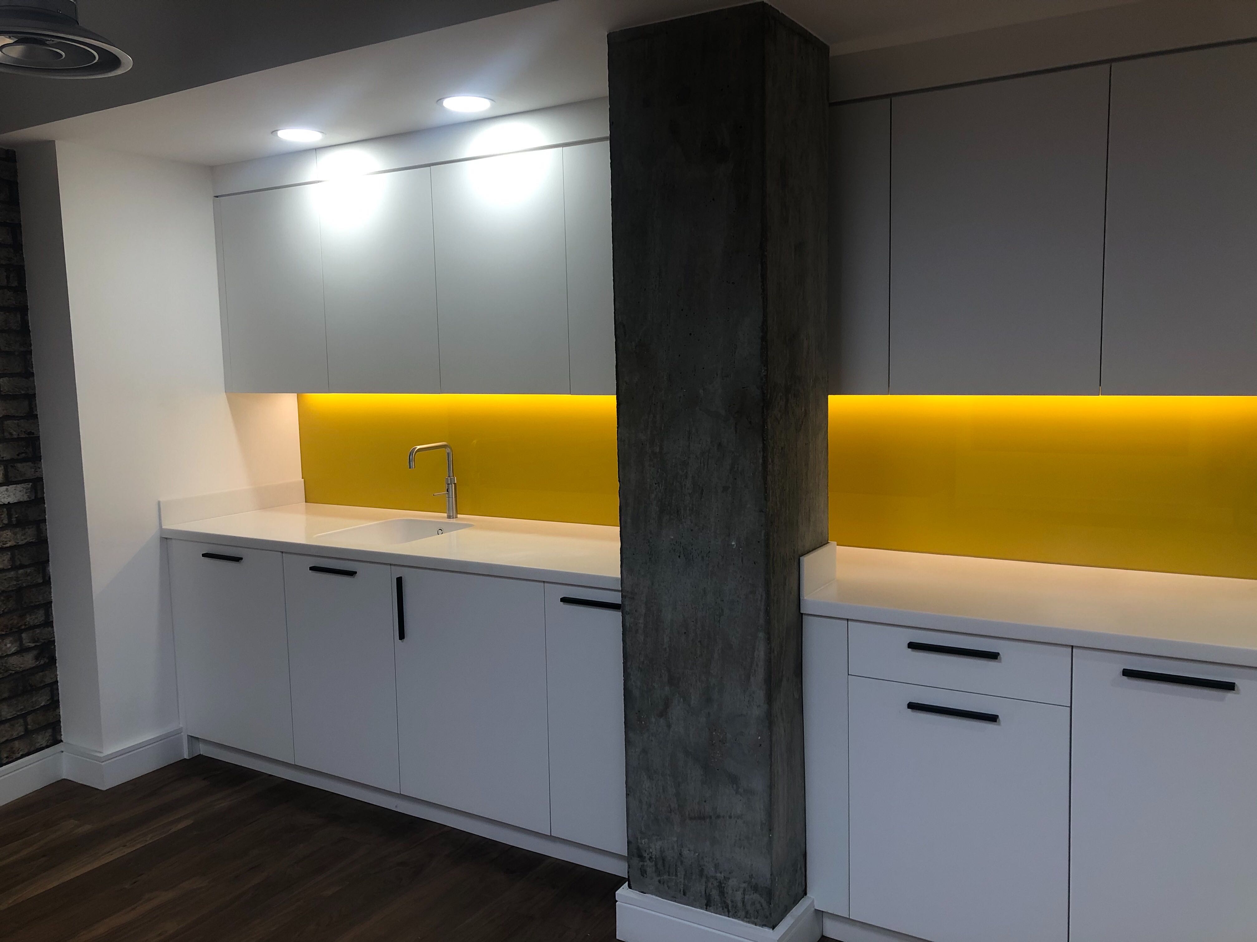 Modern kitchenette with white cabinetry and yellow backlighting for events and meetings.