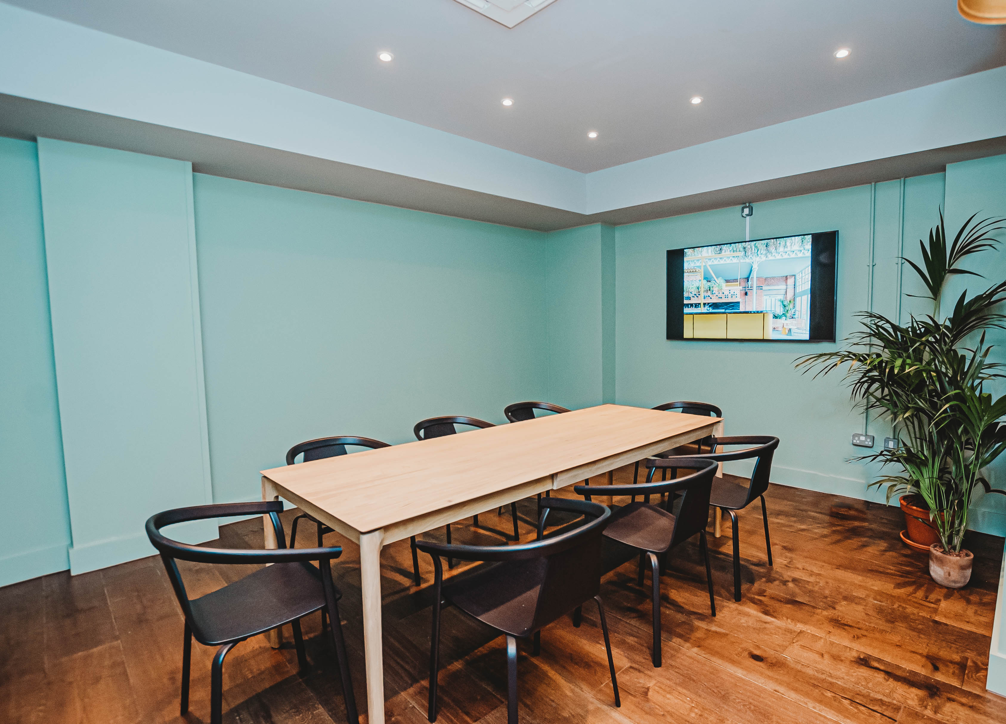 Modern meeting room with wooden table and mint-green walls for collaborative events.
