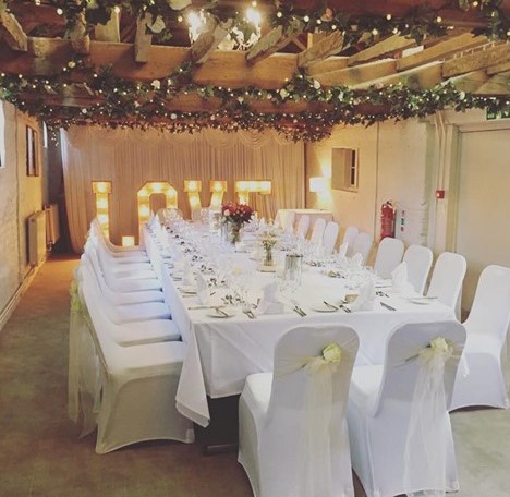 Elegant wedding banquet setup at The Surrey Barns with floral centerpieces and "LOVE" lights.