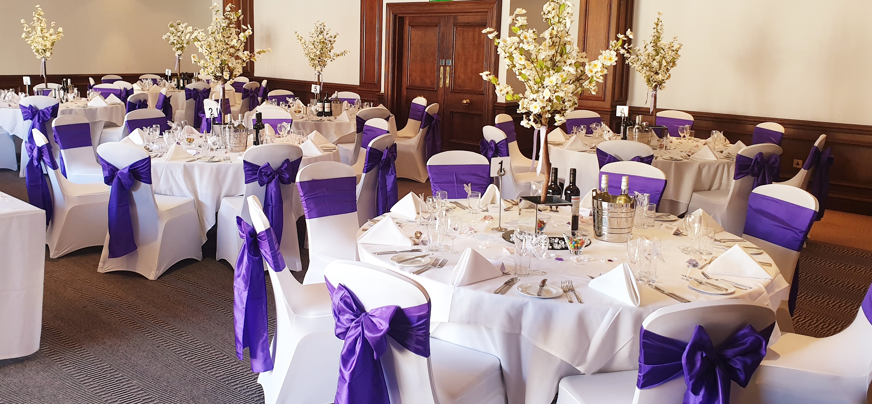 Elegant banquet hall at Holiday Inn Guildford with white tables and purple sashes for weddings.