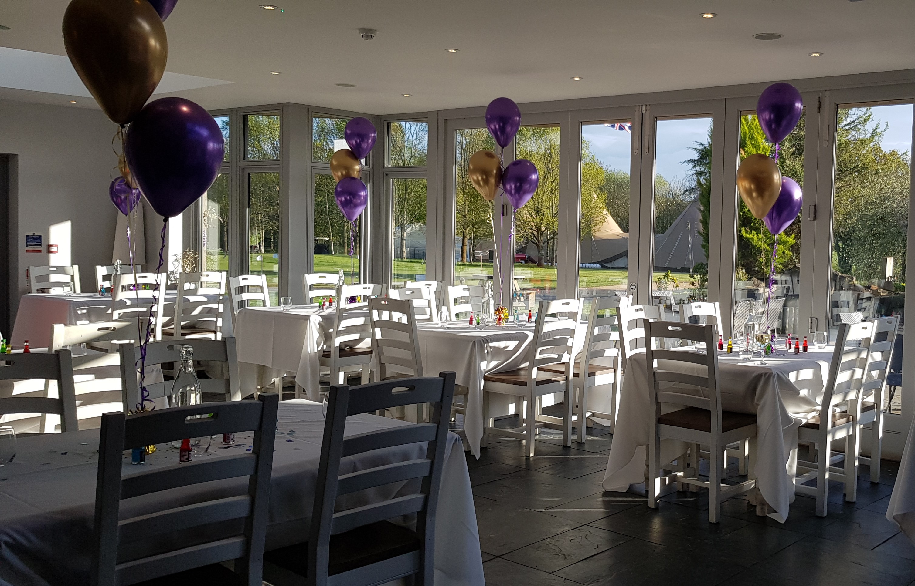 Event space at Blacknest Golf Club with white tables and colorful balloons for celebrations.
