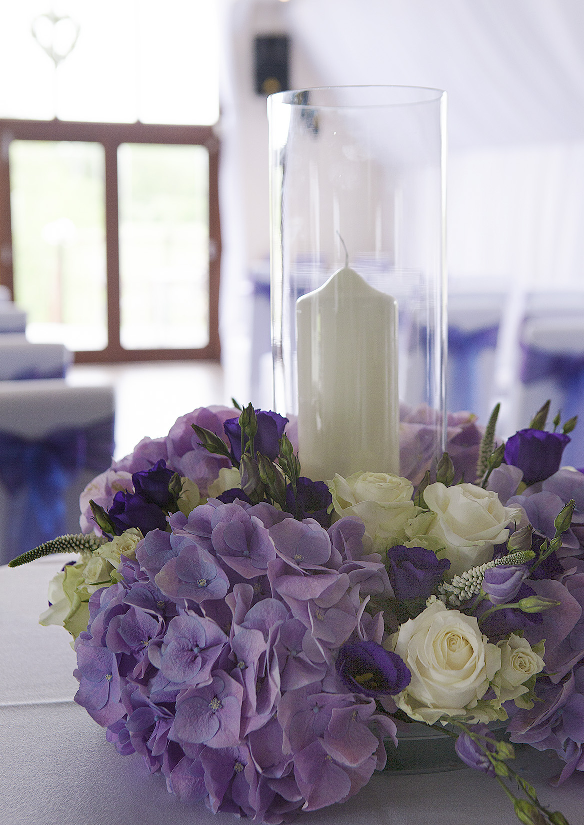 Elegant centerpiece with white candle and purple flowers for weddings and upscale events.