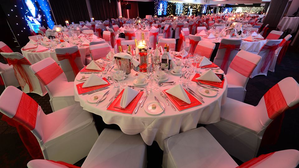 Banquet setup with round tables and red accents at Ashton Gate Stadium for weddings or events.