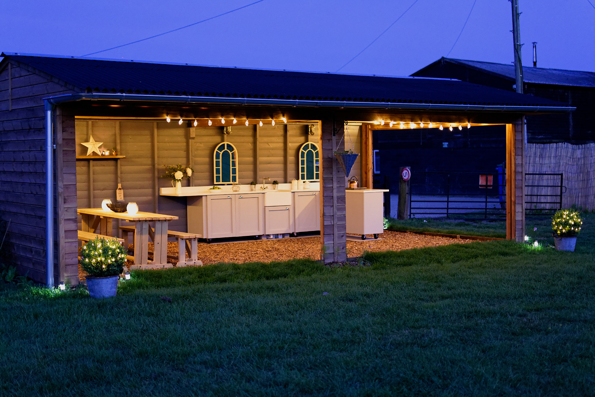 Glamping field with rustic kitchen and string lights for outdoor culinary events.
