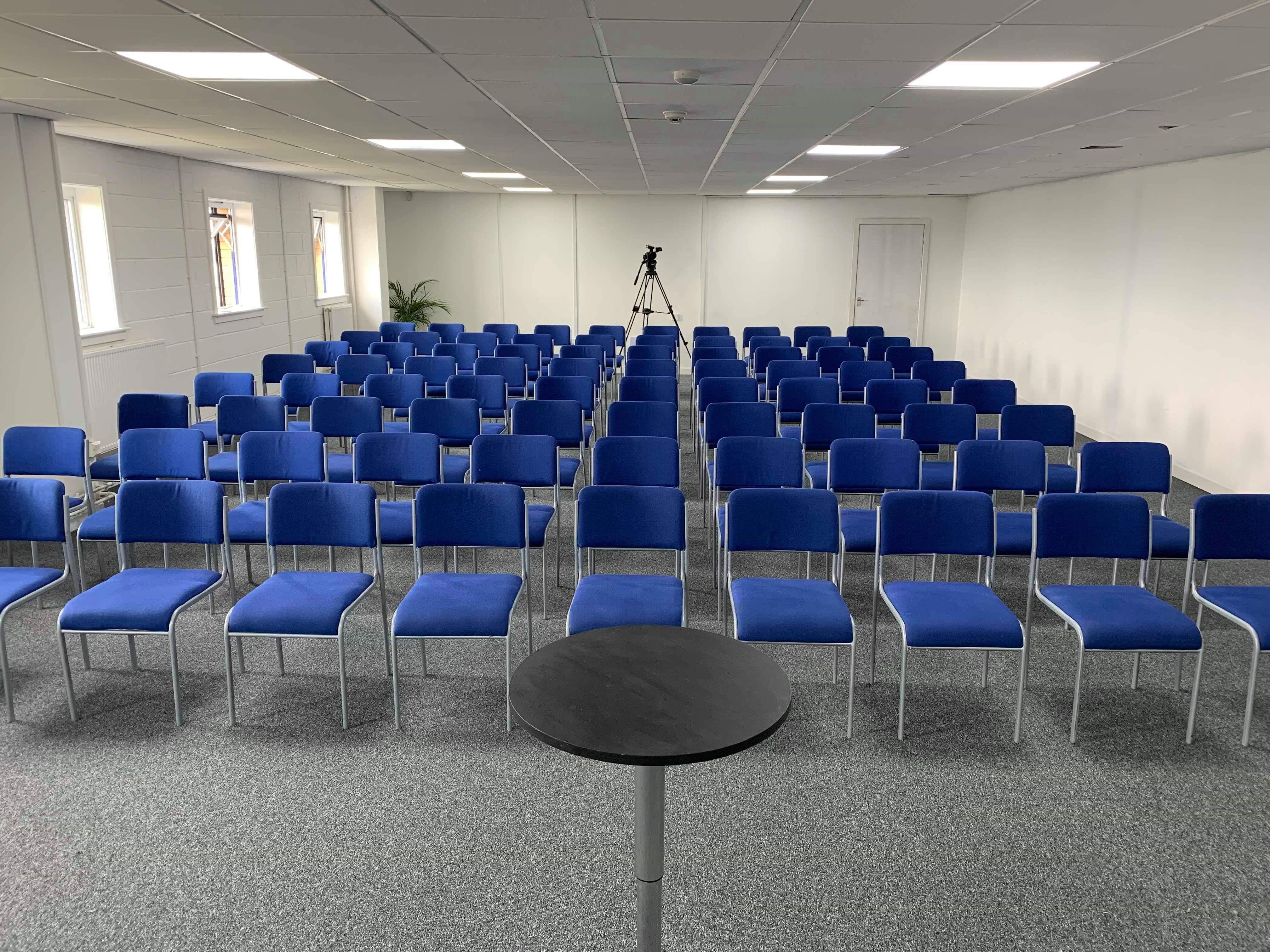 Auditorium with blue chairs and podium, perfect for presentations and workshops.