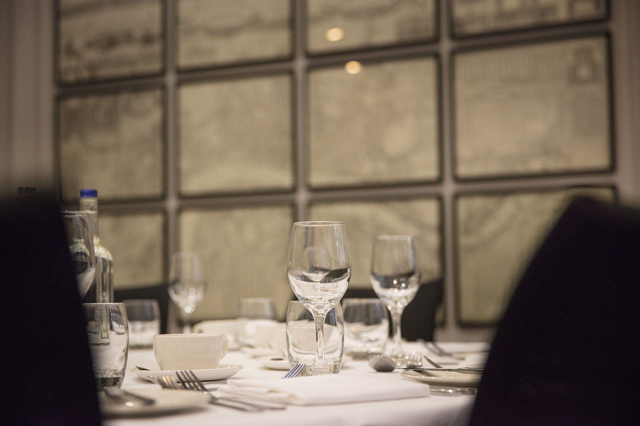 Elegant dining table setup for corporate dinner with glassware and framed maps.