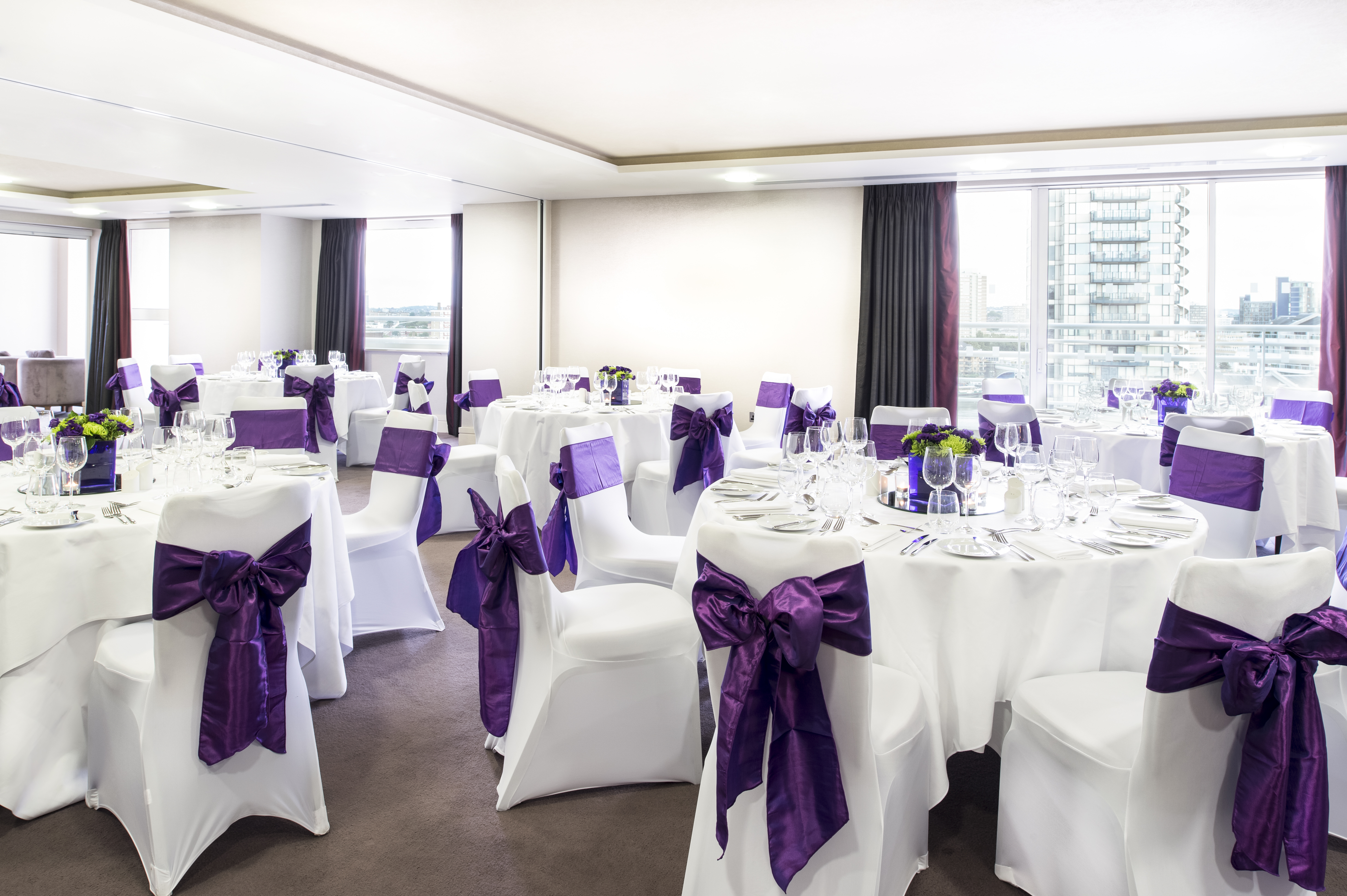Elegant event space in Chelsea Harbour Hotel with white linens and purple sashes.