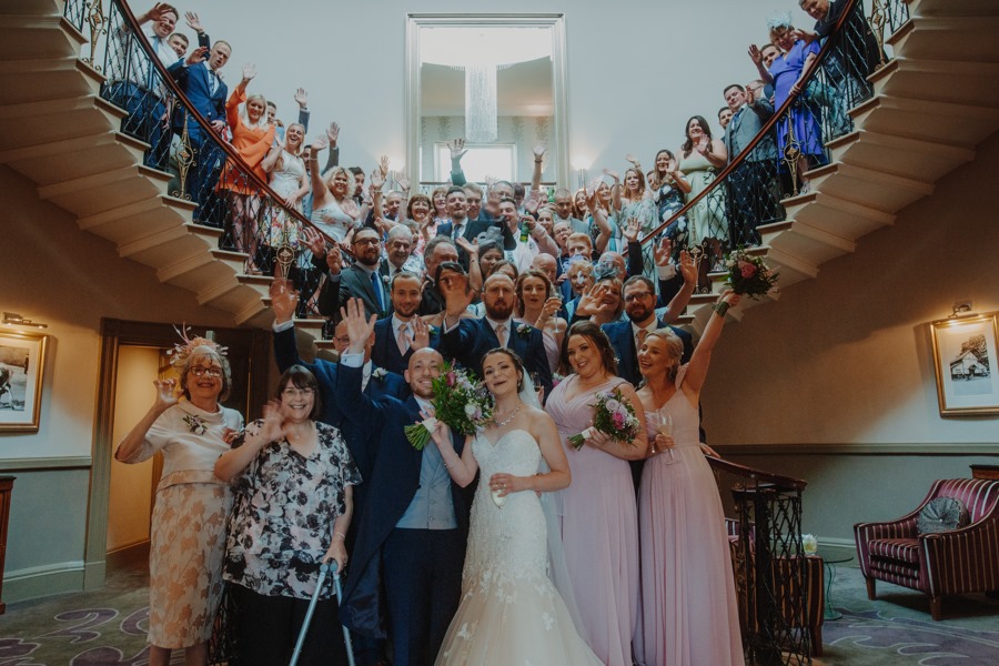 Vibrant wedding celebration on grand staircase at The Mansion, showcasing joyful guests.