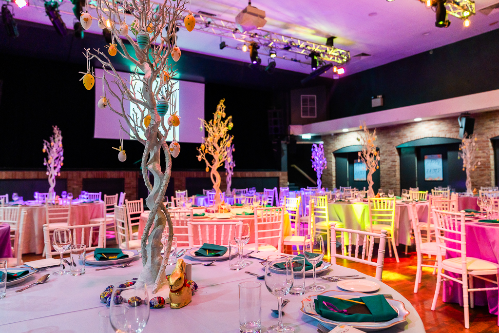 Easter gala ballroom, pink/purple uplighting, egg tree centerpiece.