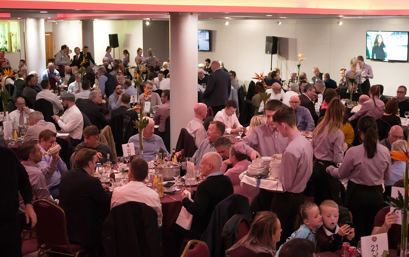 Gorgie Suite event space with round tables, lively dinner atmosphere, and audio-visual setup.