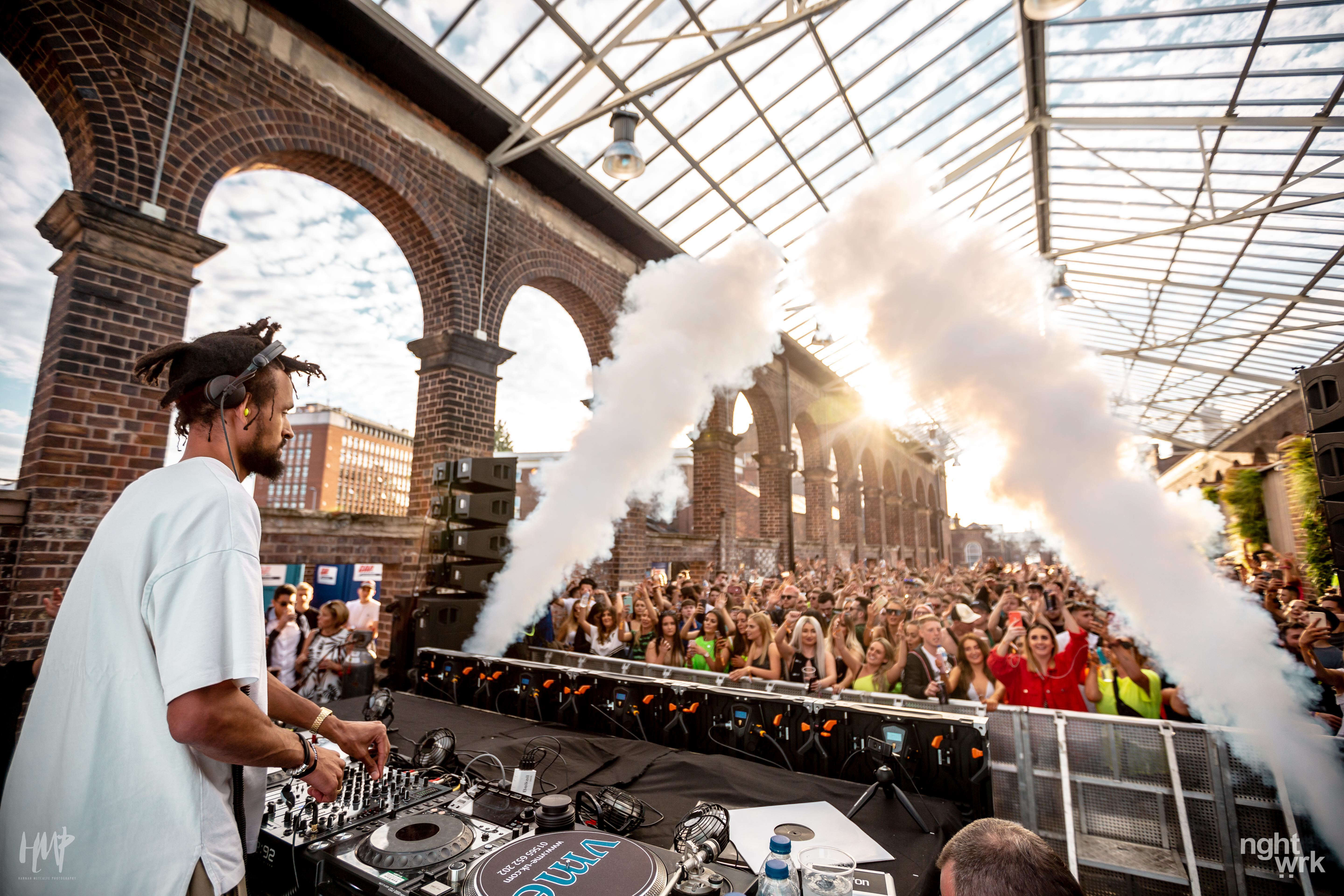 Vibrant outdoor DJ event at The Carriage Shed with dramatic lighting and smoke effects.
