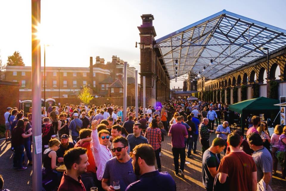 Vibrant outdoor networking event at The Carriage Shed with large crowd under open-air structure.