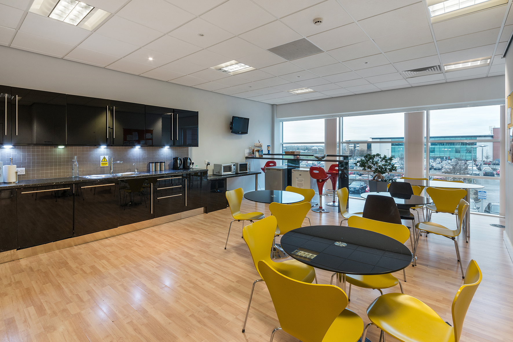 Modern break room in Qora with sleek black cabinetry and vibrant yellow chairs for events.