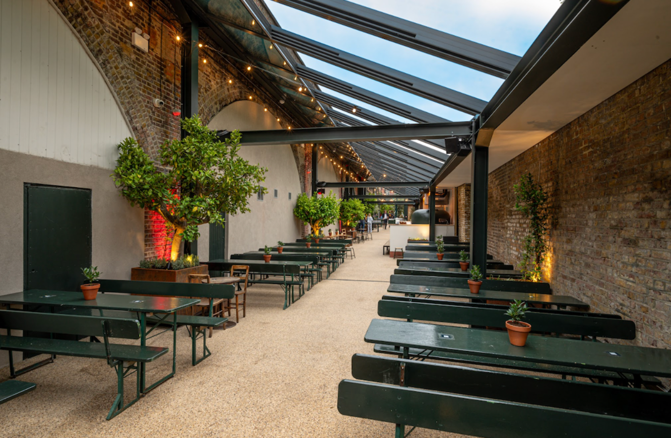 Spacious event space with communal tables and greenery, perfect for gatherings and workshops.