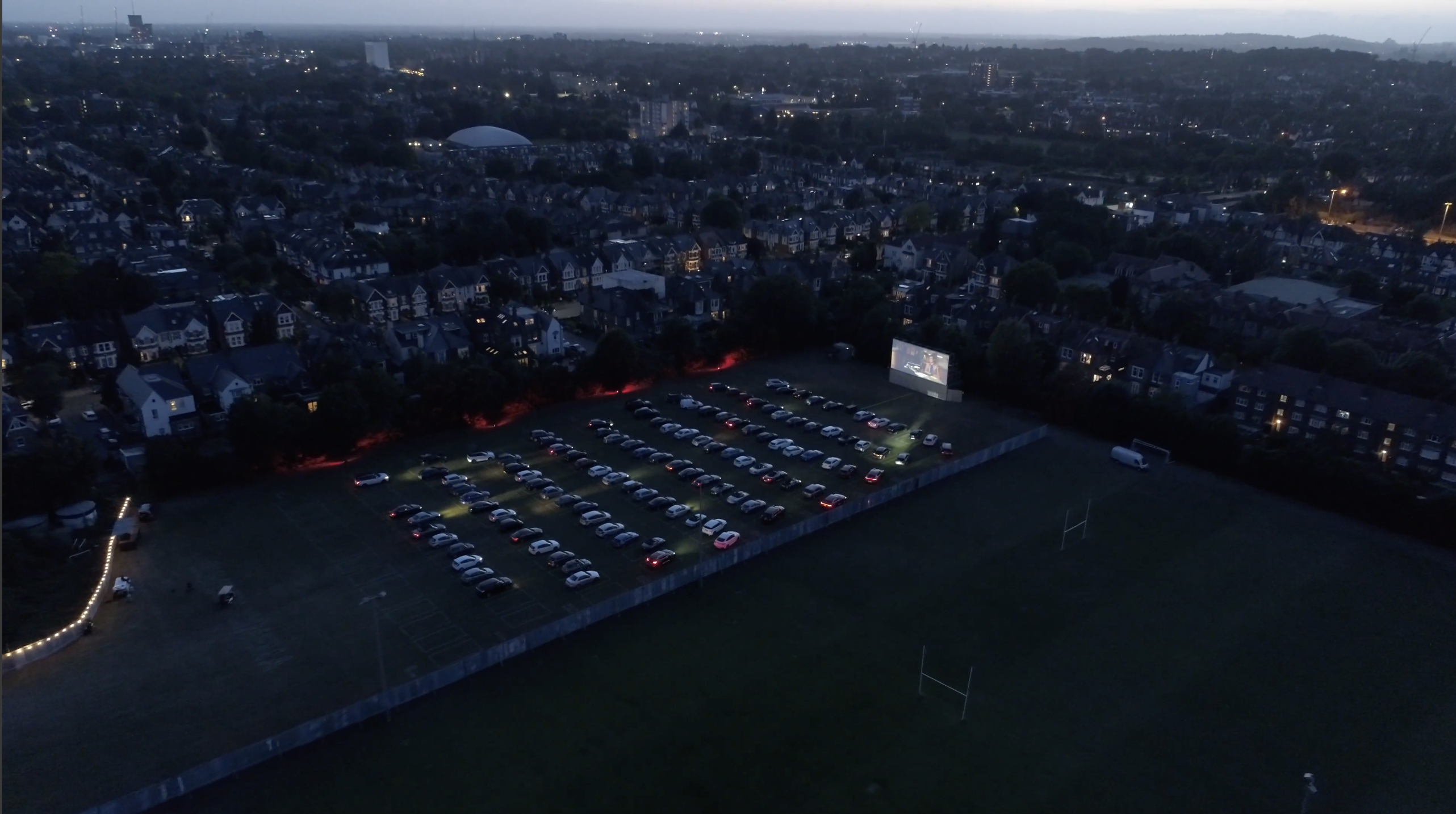 Drive-in movie setup at Sunset Cinema with large screen and parked cars for community events.