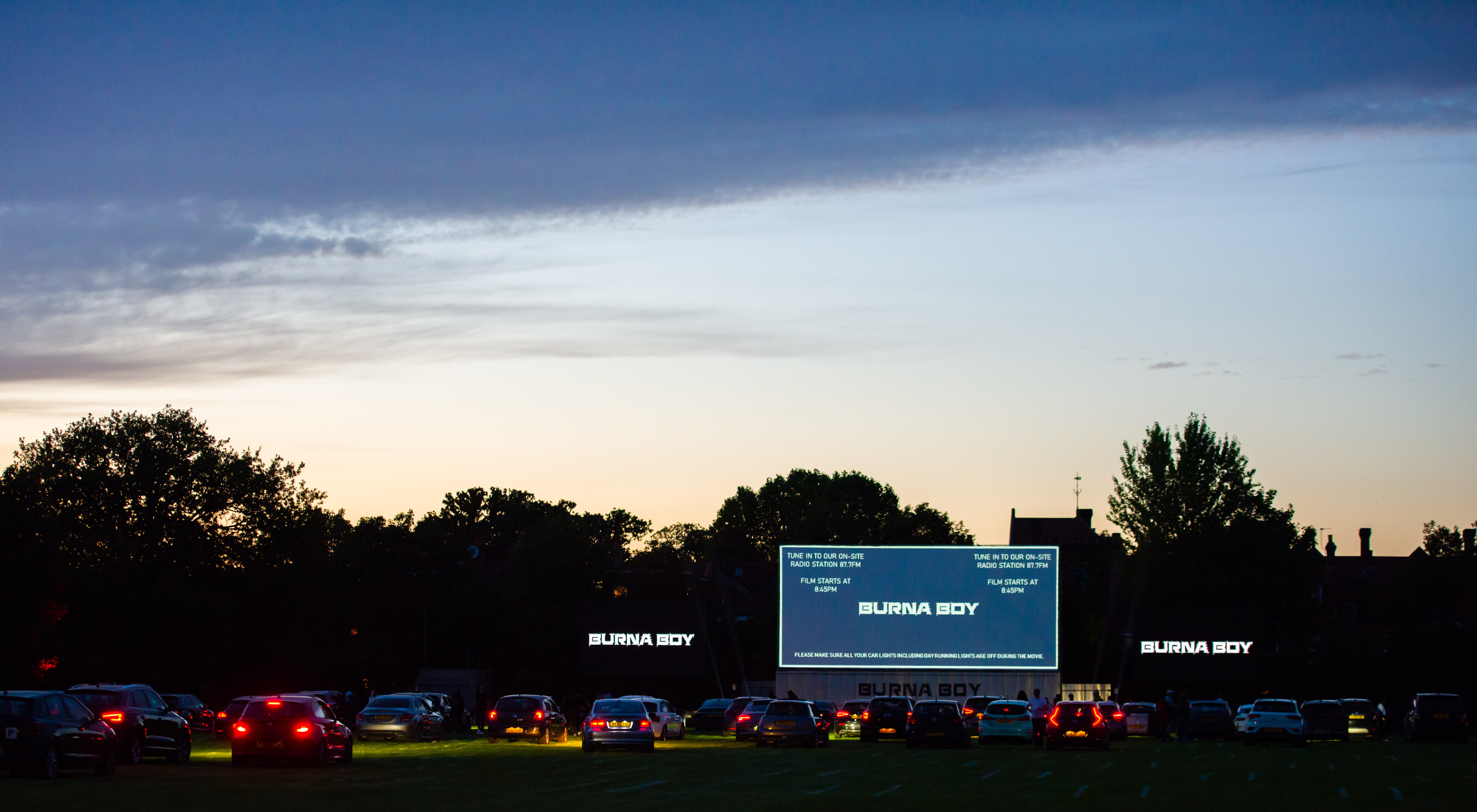 Drive-in event at Sunset Cinema with large screen and cars under twilight sky.