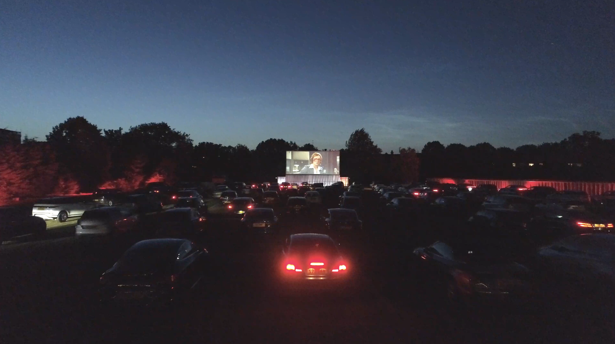 Vibrant outdoor movie event at Sunset Cinema with cars and large screen.