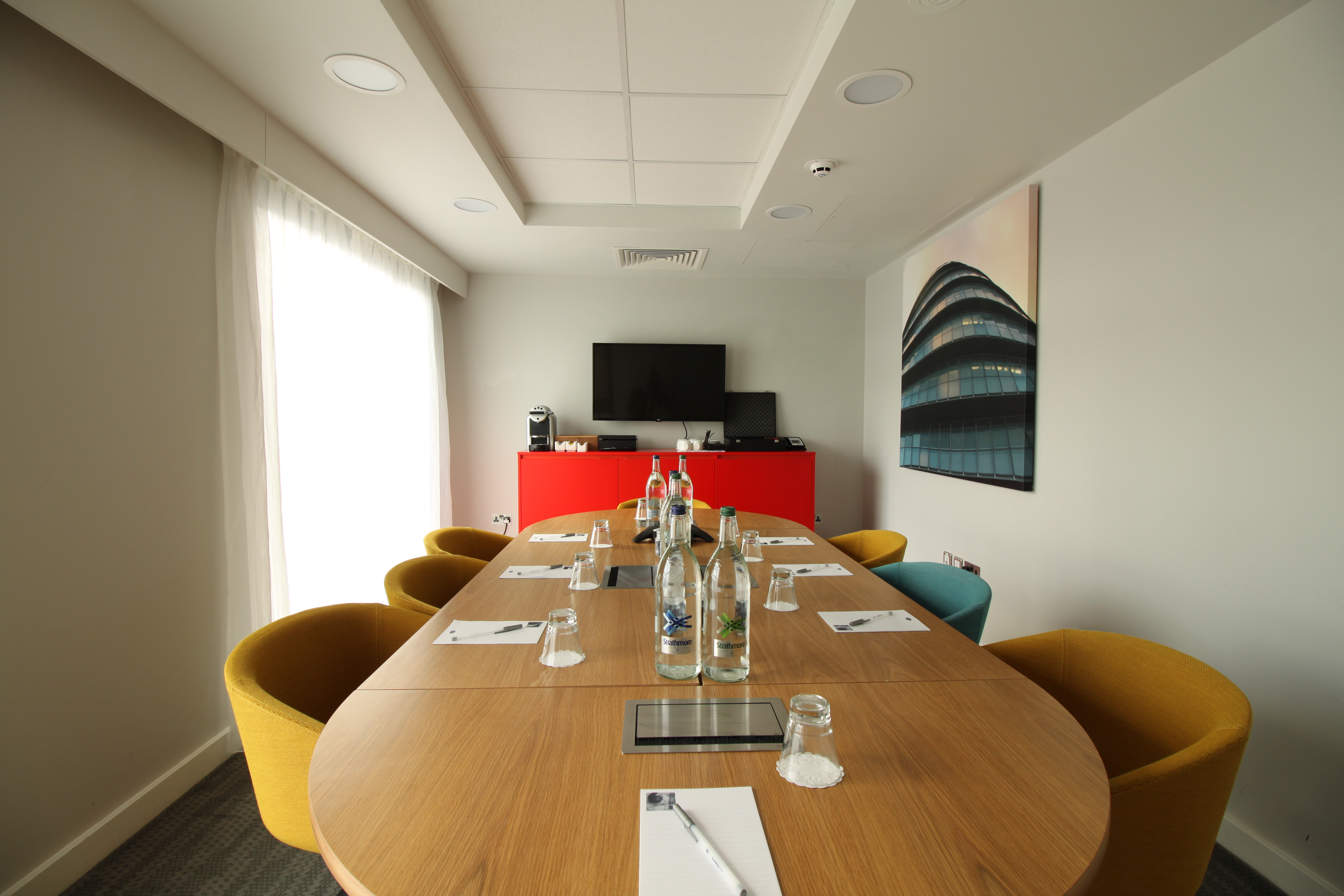Modern meeting room at Hampton by Hilton London Docklands with oval table and vibrant chairs.