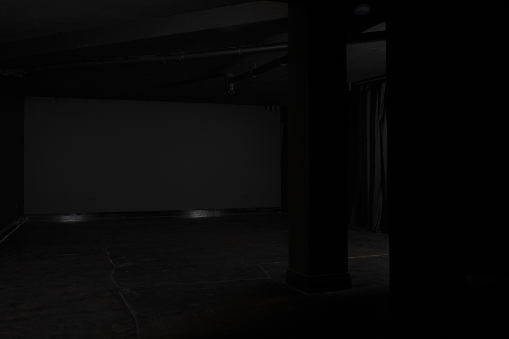 Dimly lit Blackout studio venue with blank screen for presentations and workshops.