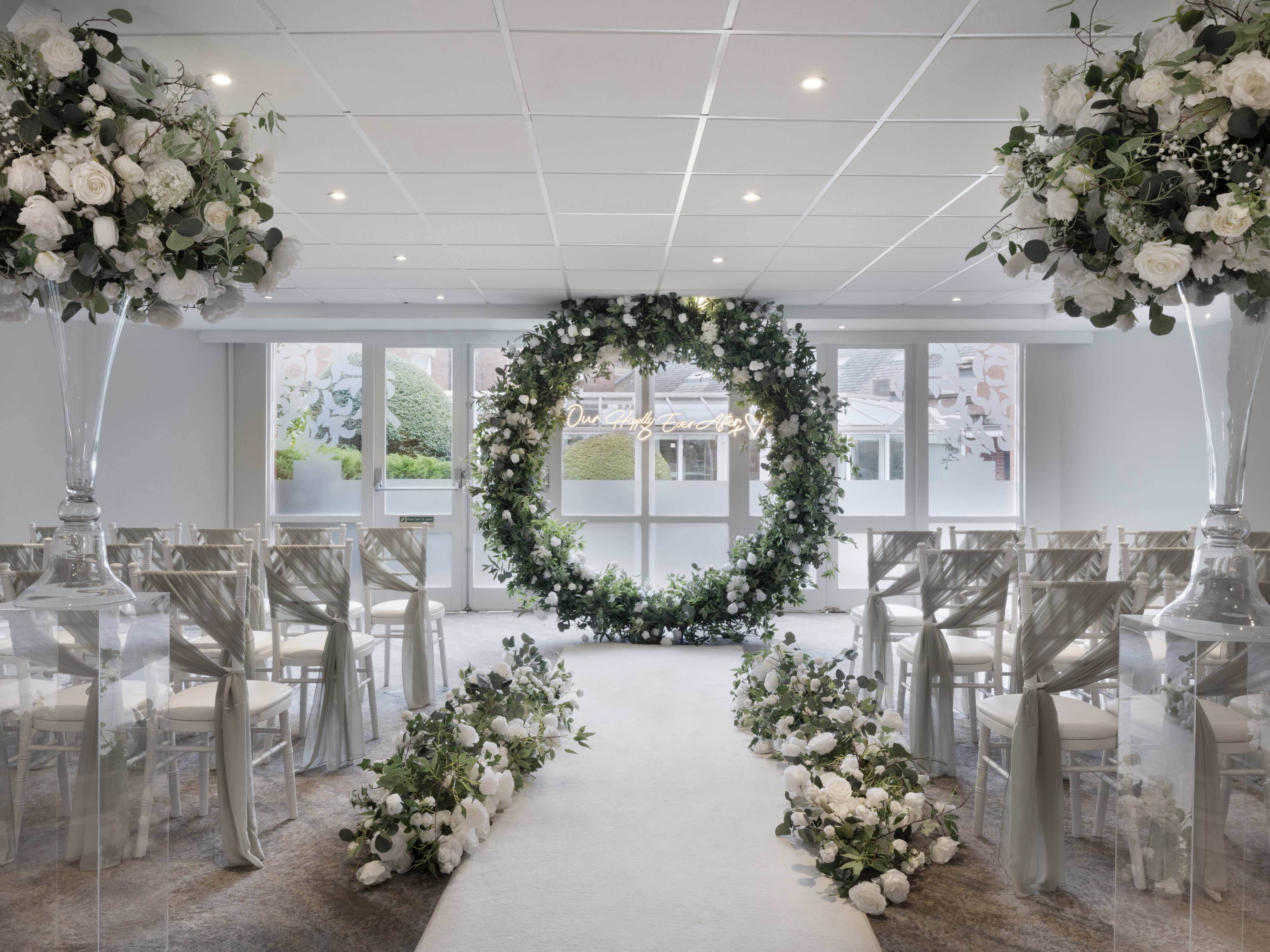 Elegant wedding venue at Delta Hotels, featuring floral backdrop and clear chairs.