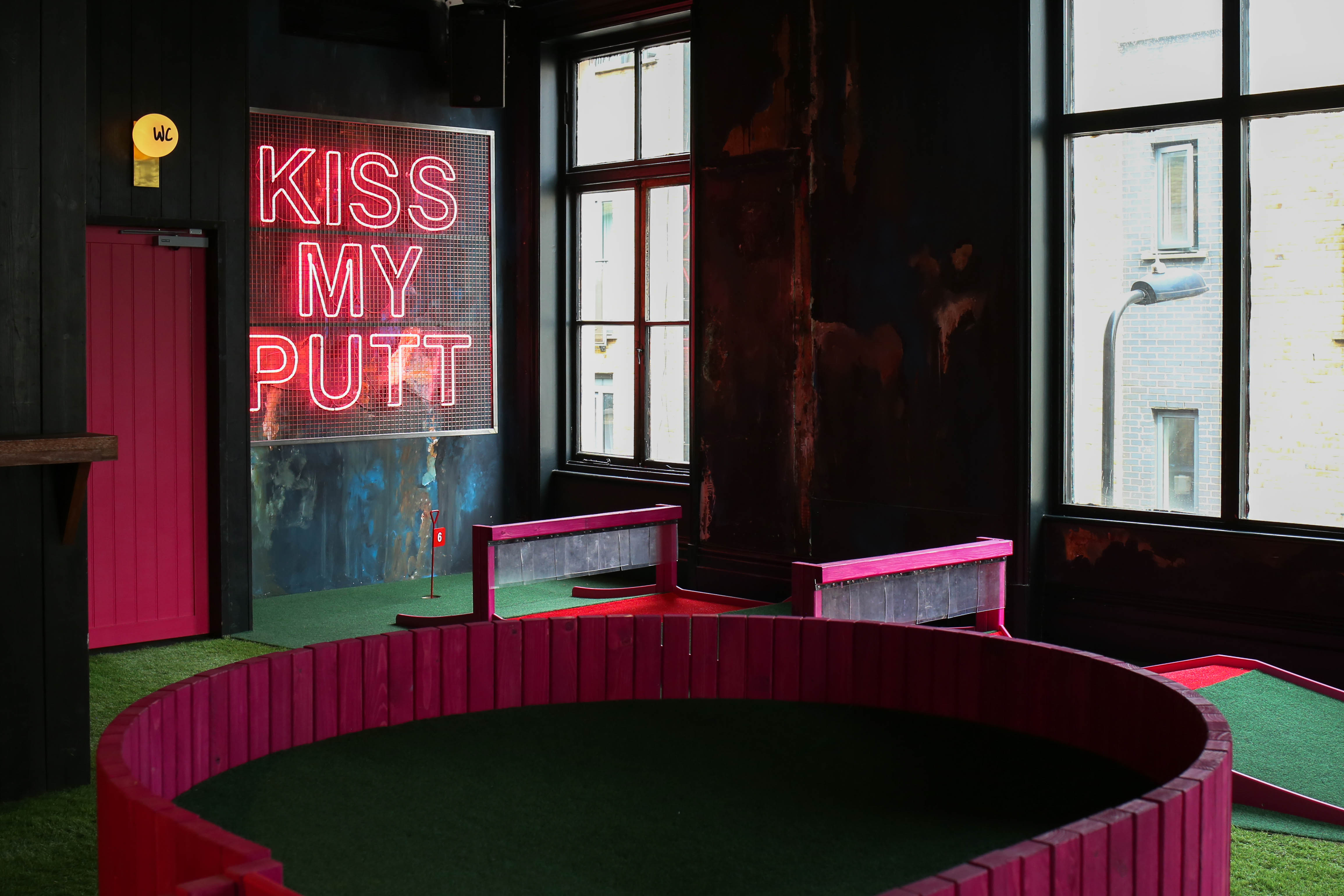 Vibrant mini-golf venue in Shoreditch with neon "KISS MY PUTT" sign for events.