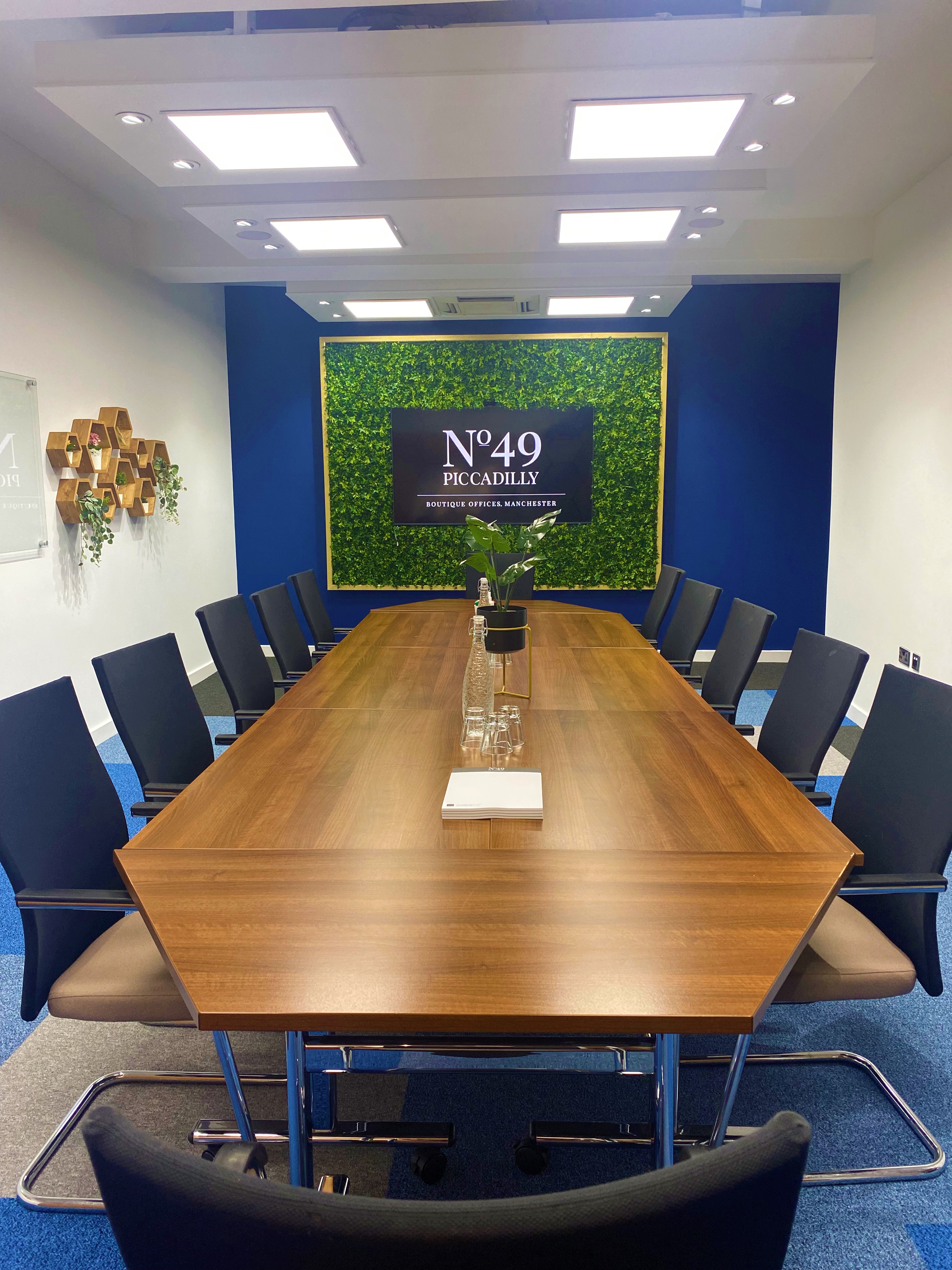 Modern meeting room at Crompton, featuring a long wooden table and greenery. Ideal for presentations.