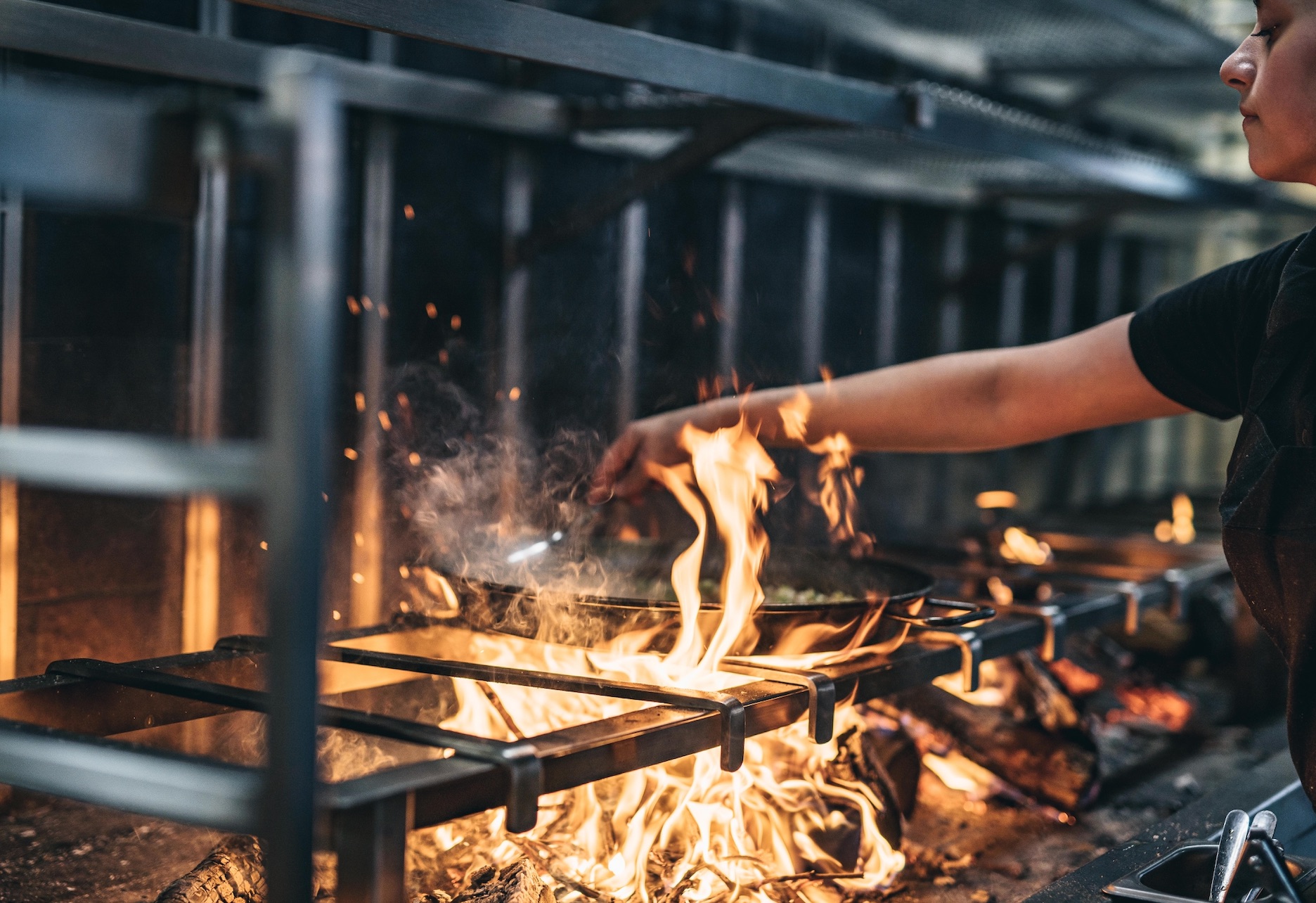Chef managing open flame in Arros QD dining room for event catering safety.