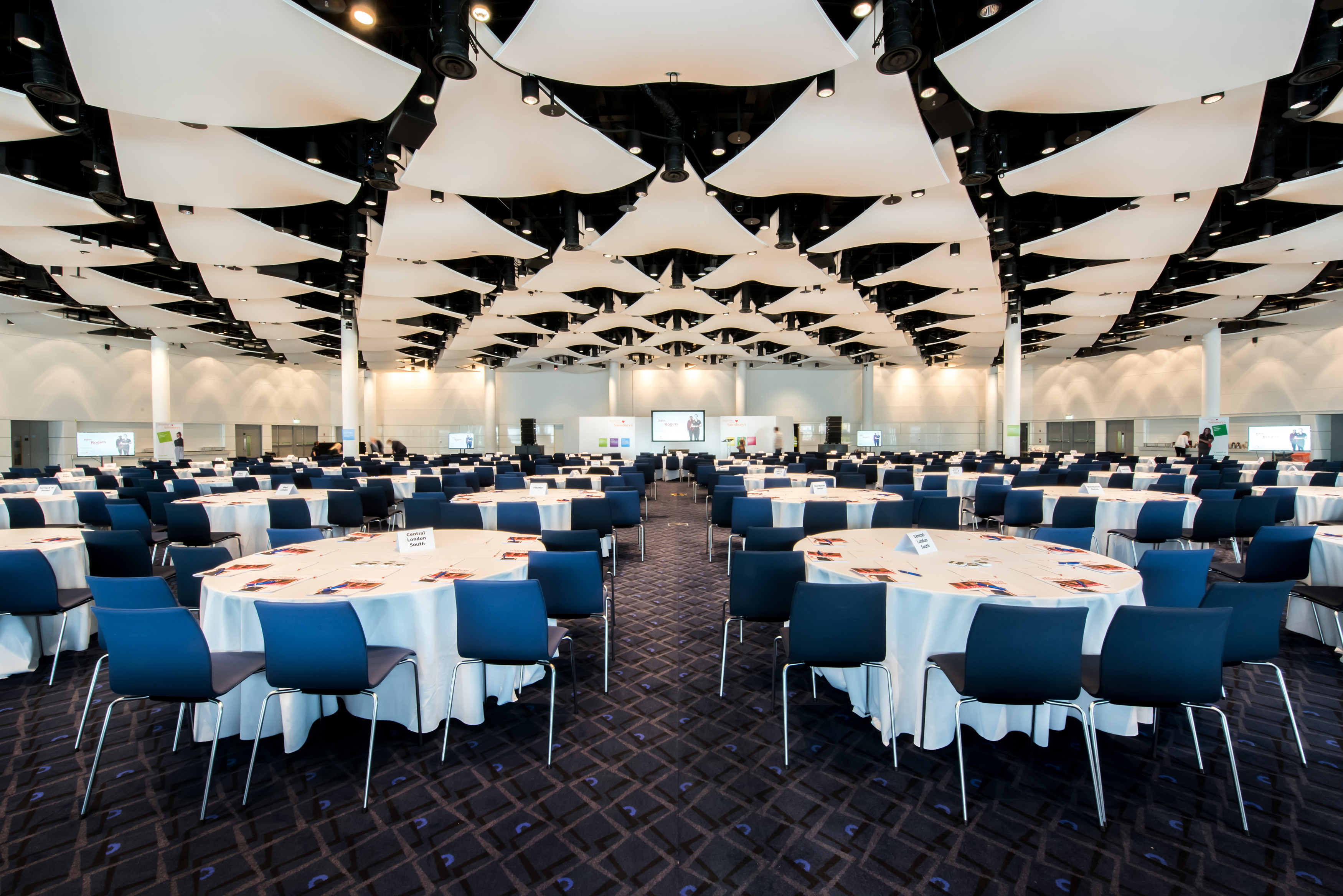 Wembley Stadium Great Hall set for elegant conference with round tables and blue chairs.