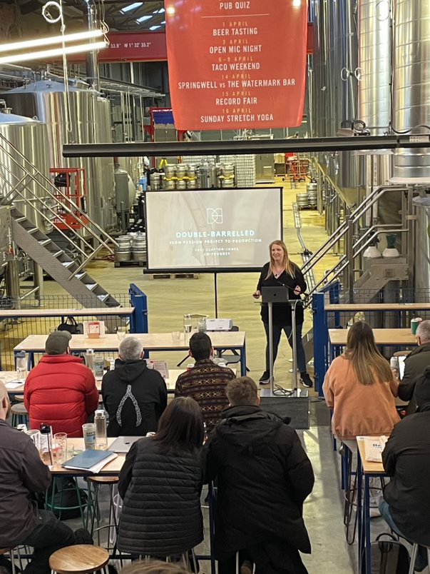 Speaker at North Brewing Co. event with engaged audience in industrial brewery setting.