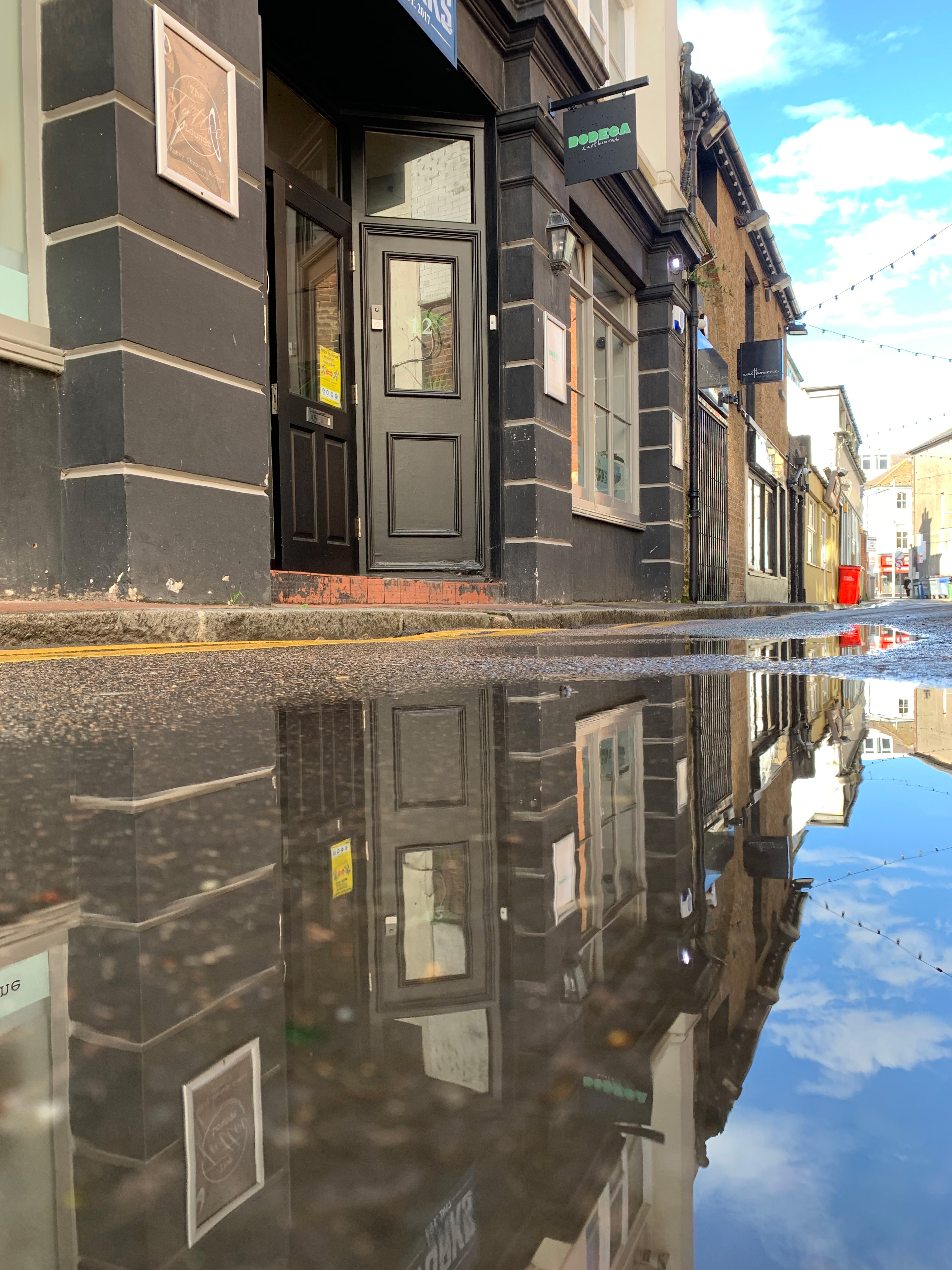 Reflective puddle on cobblestone street at Bodega Eastbourne, ideal for events and photography.
