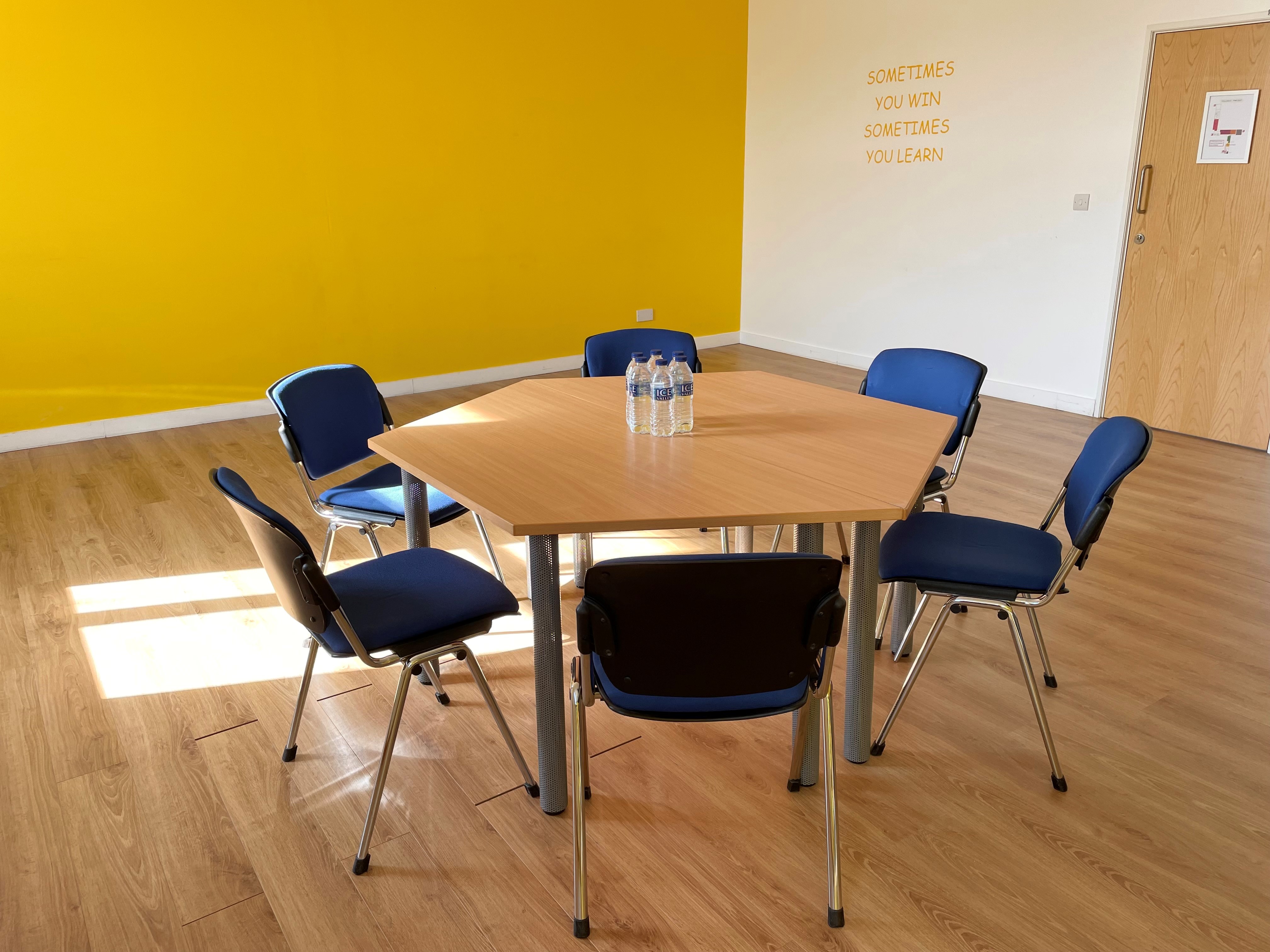 Bright yellow meeting room with hexagonal table and blue chairs, perfect for workshops.