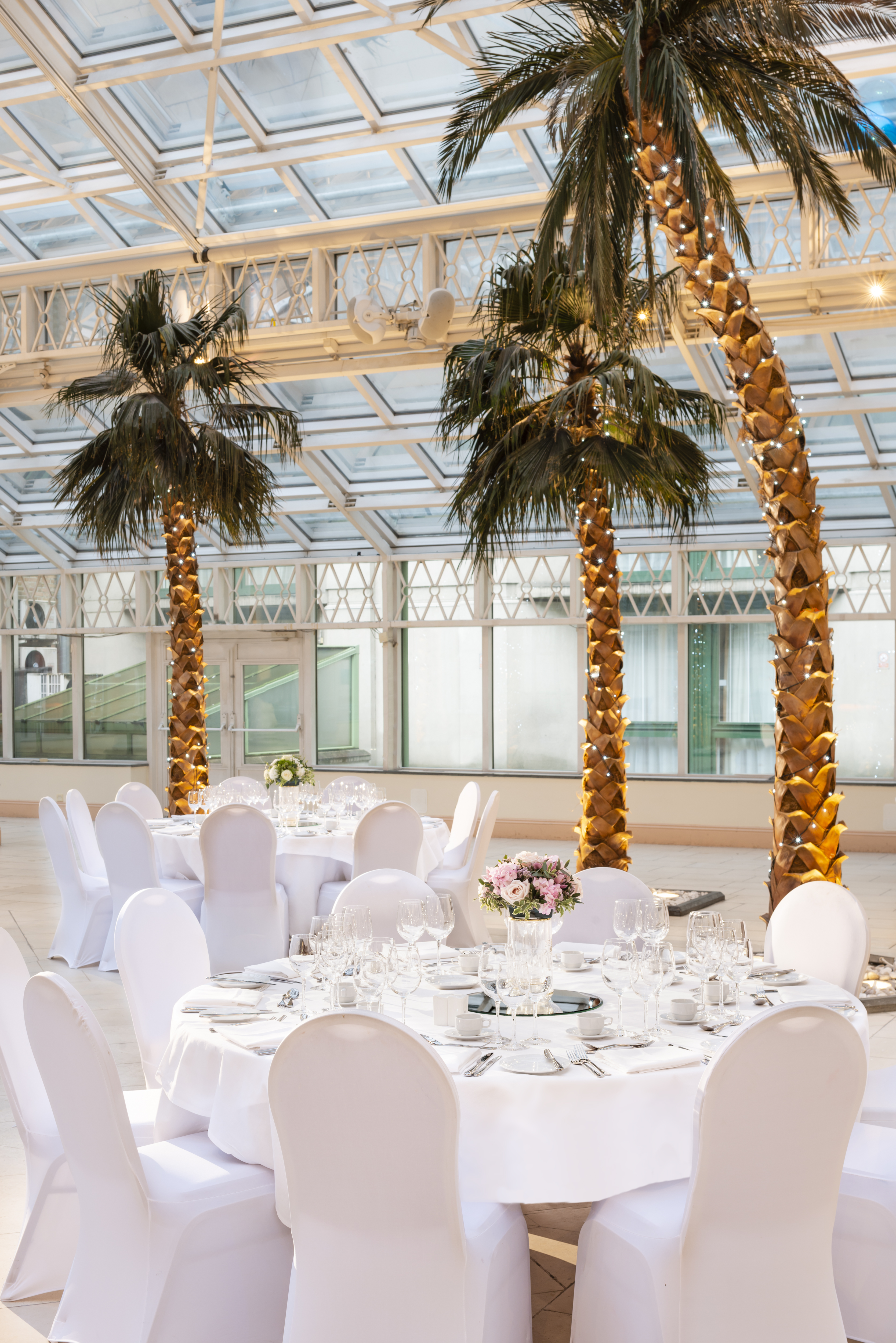 Elegant event space with round tables and palm trees in Millennium Gloucester, London.