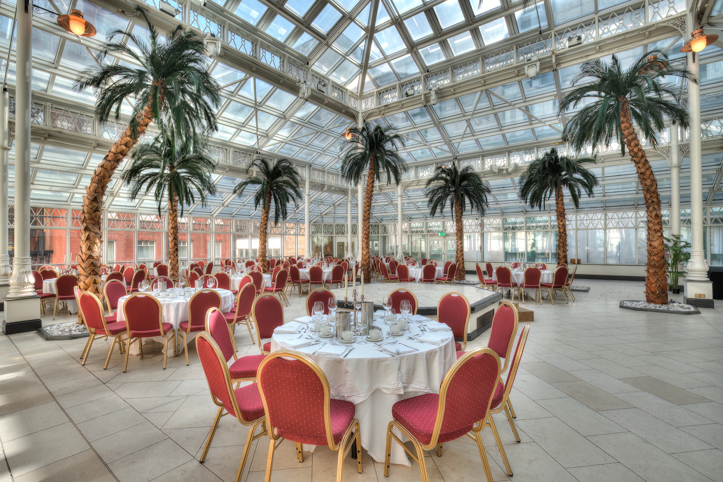 Elegant event space with round tables and palm trees in Millennium Gloucester, London.