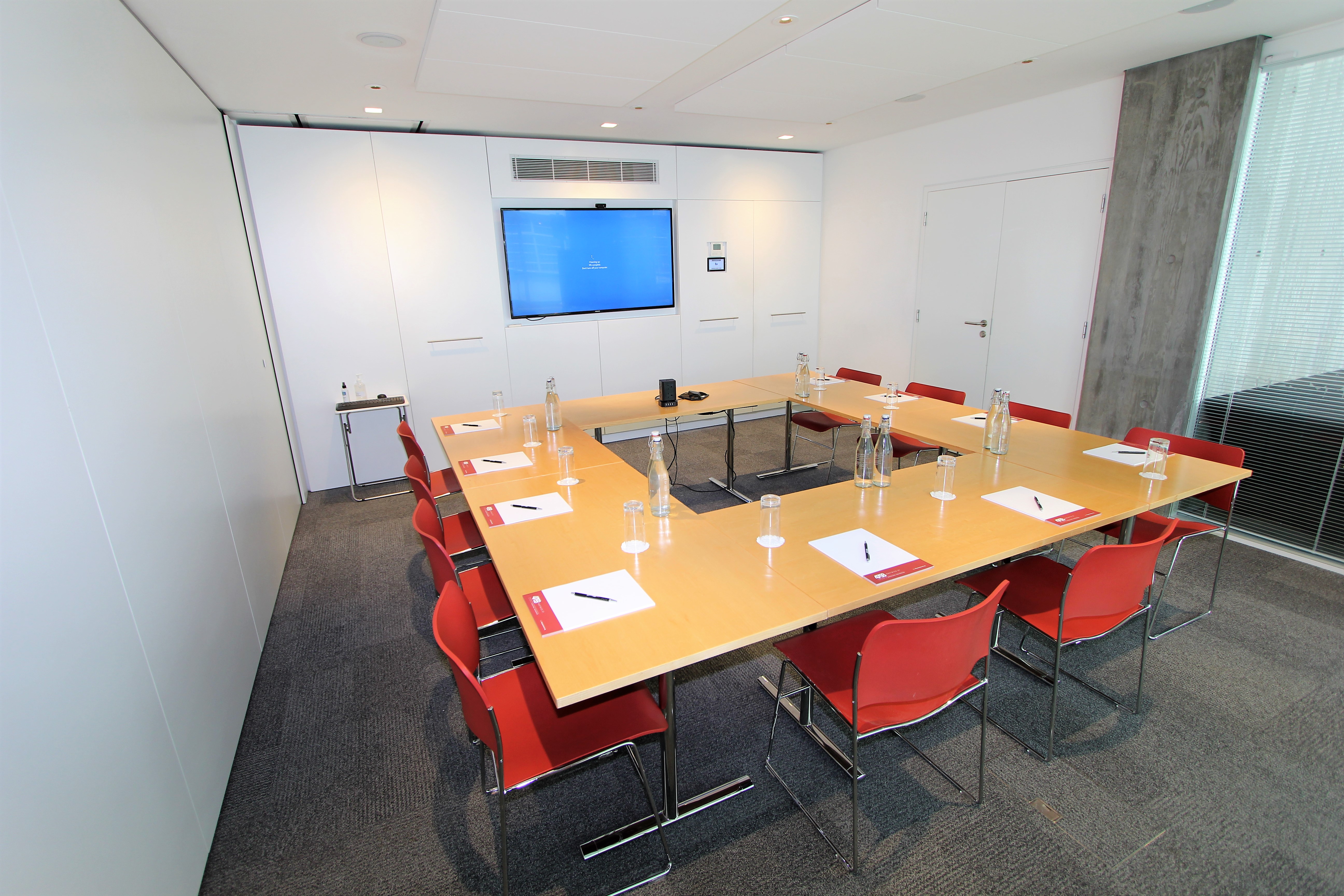 Modern meeting room with large table and red chairs, perfect for corporate events.