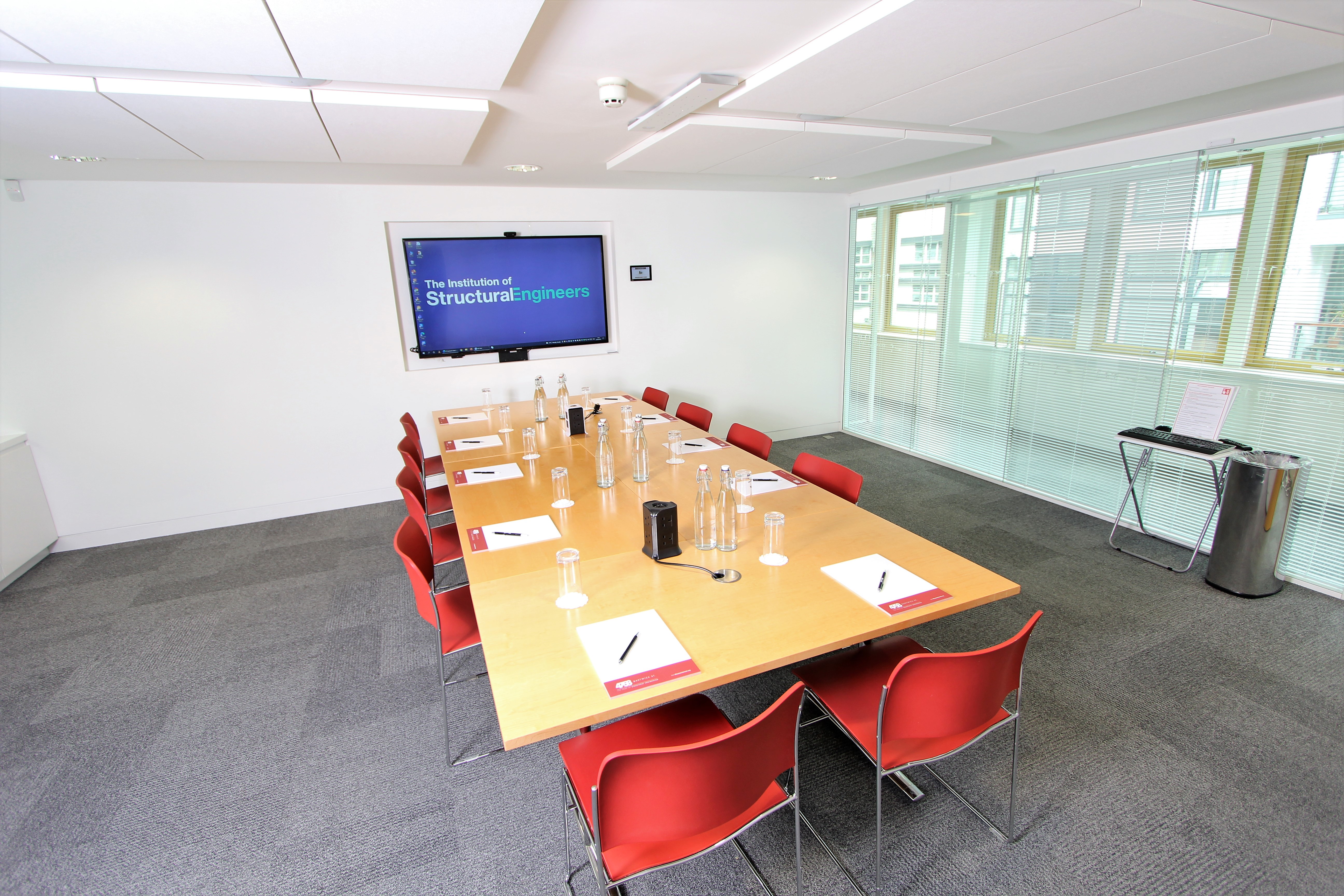 Modern conference room with wooden table and red chairs, perfect for meetings or events.